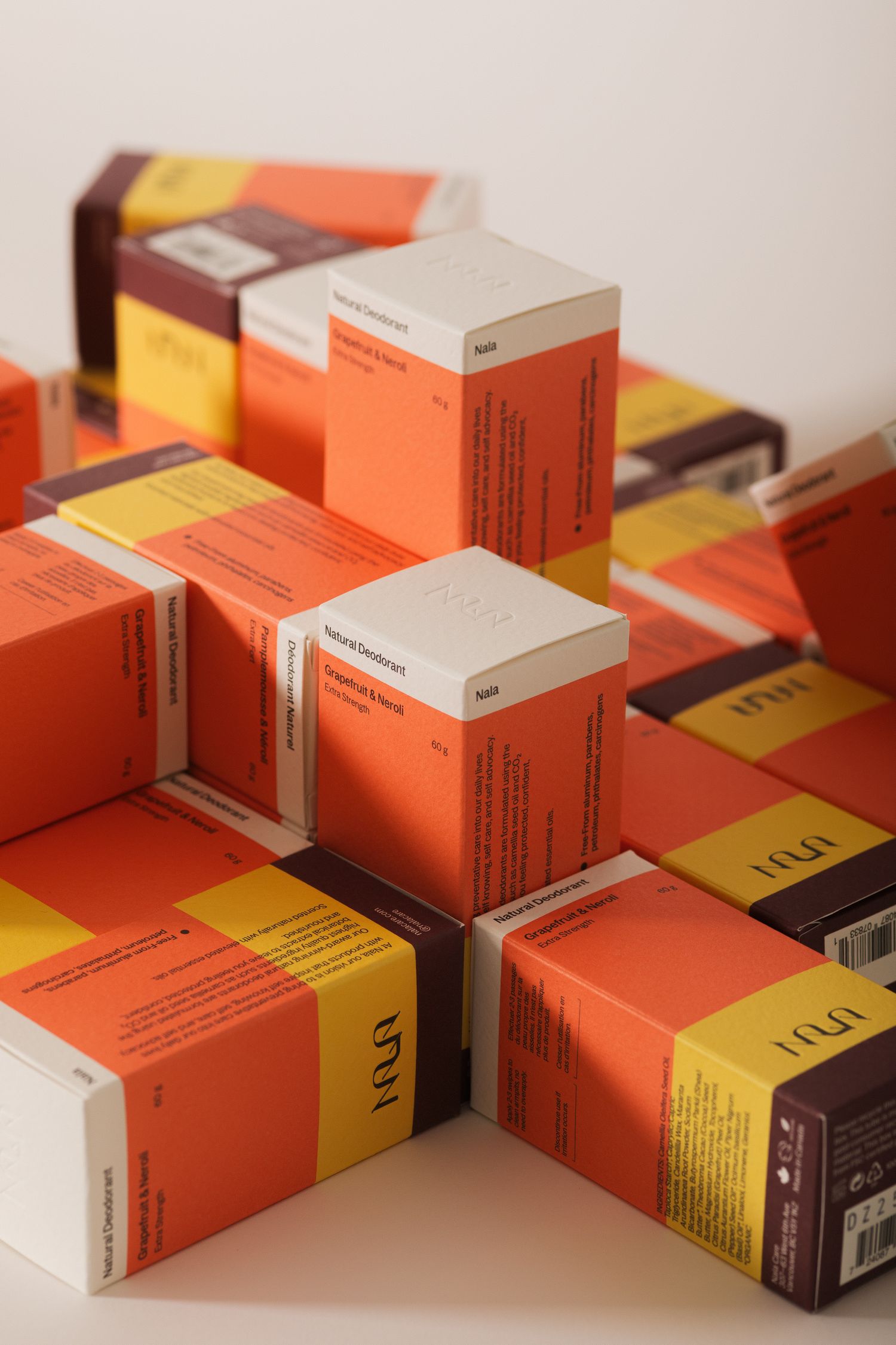Stack of Nala natural deodorant orange and yellow product boxes arranged on white surface.