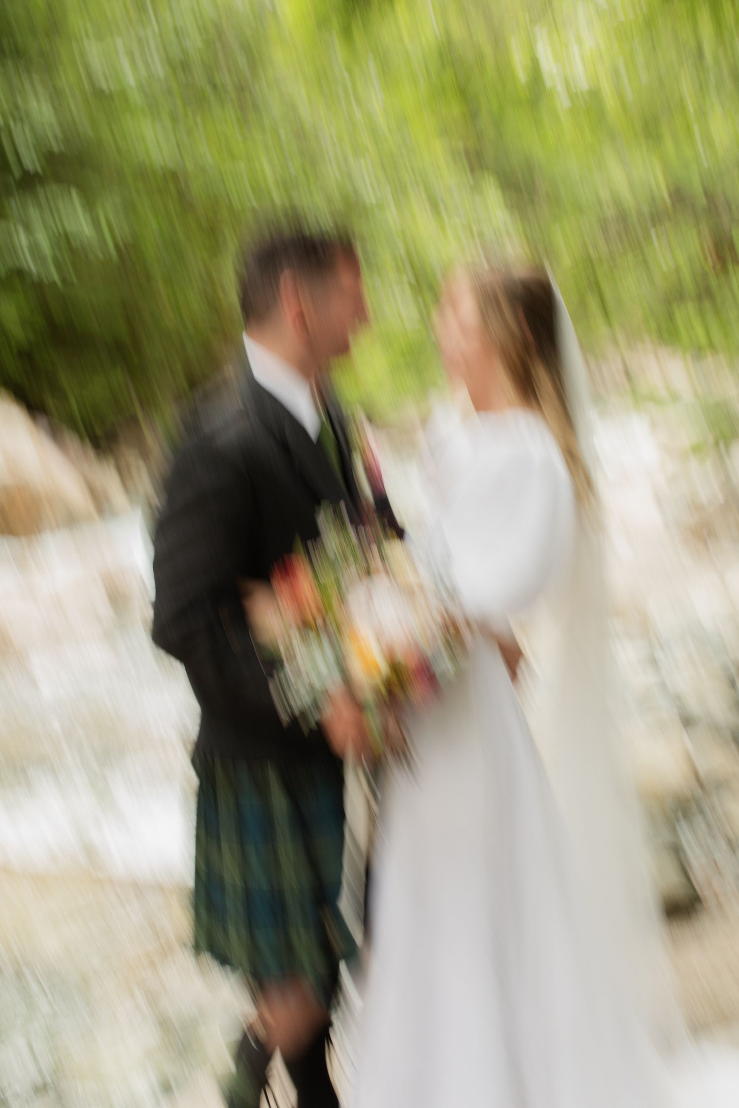 Artistic motion blur photo of bride and groom embracing outdoors in green nature setting.