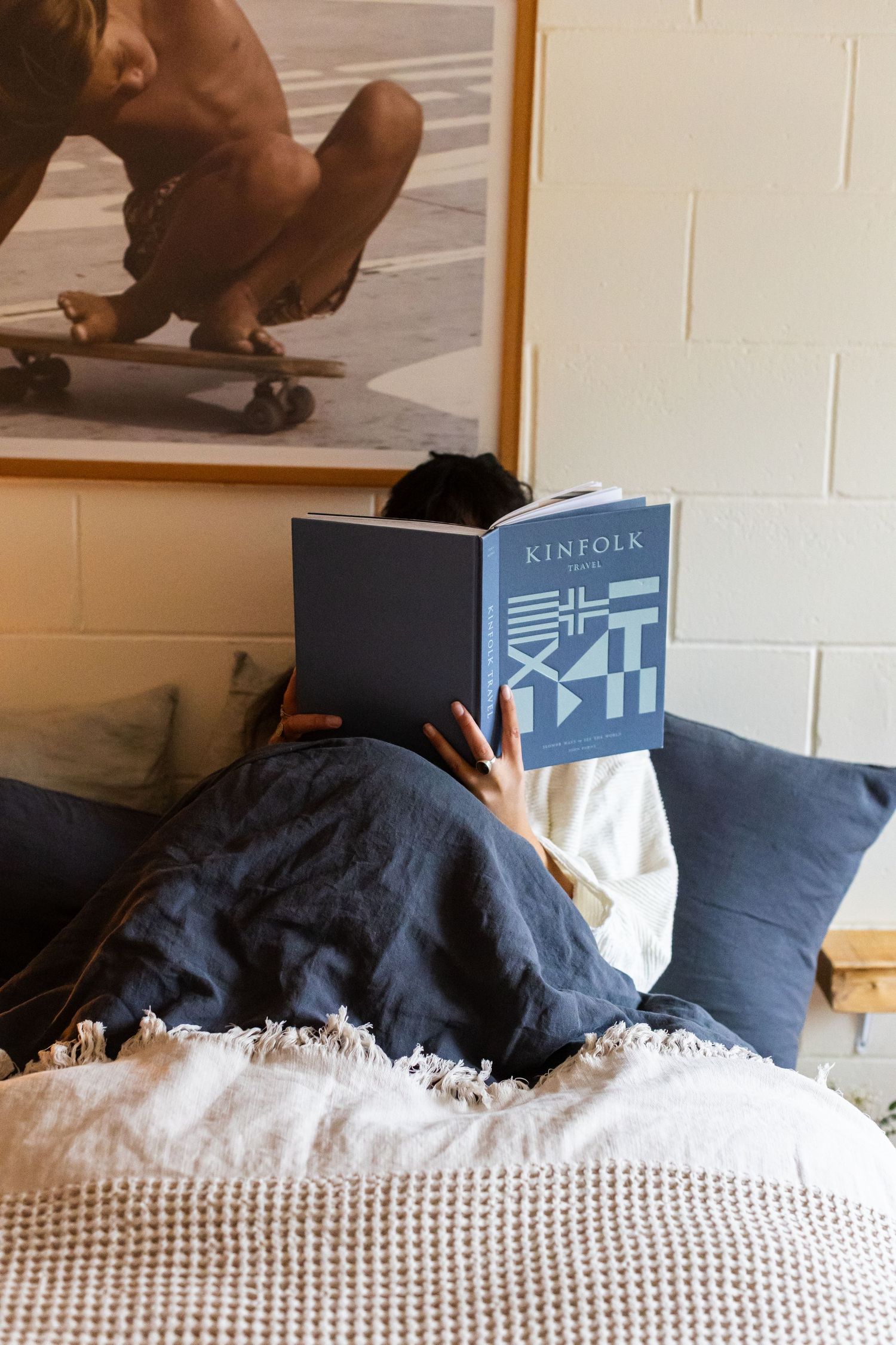Person reading a Kinfolk magazine in bed with navy linen pillows and blankets.