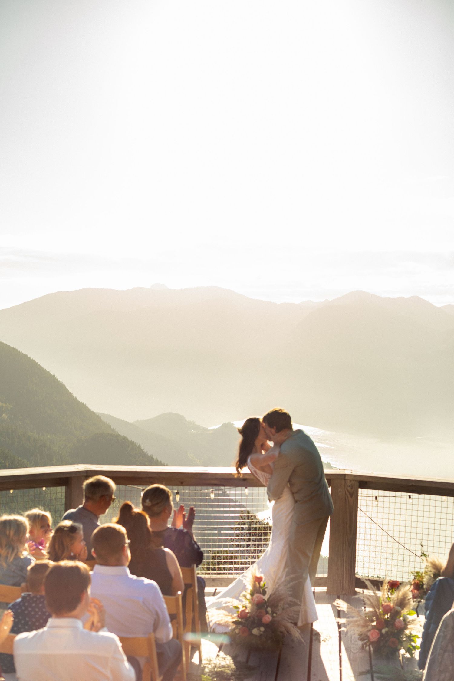 Bride and groom share a kiss at mountaintop ceremony with stunning misty mountain range backdrop.
