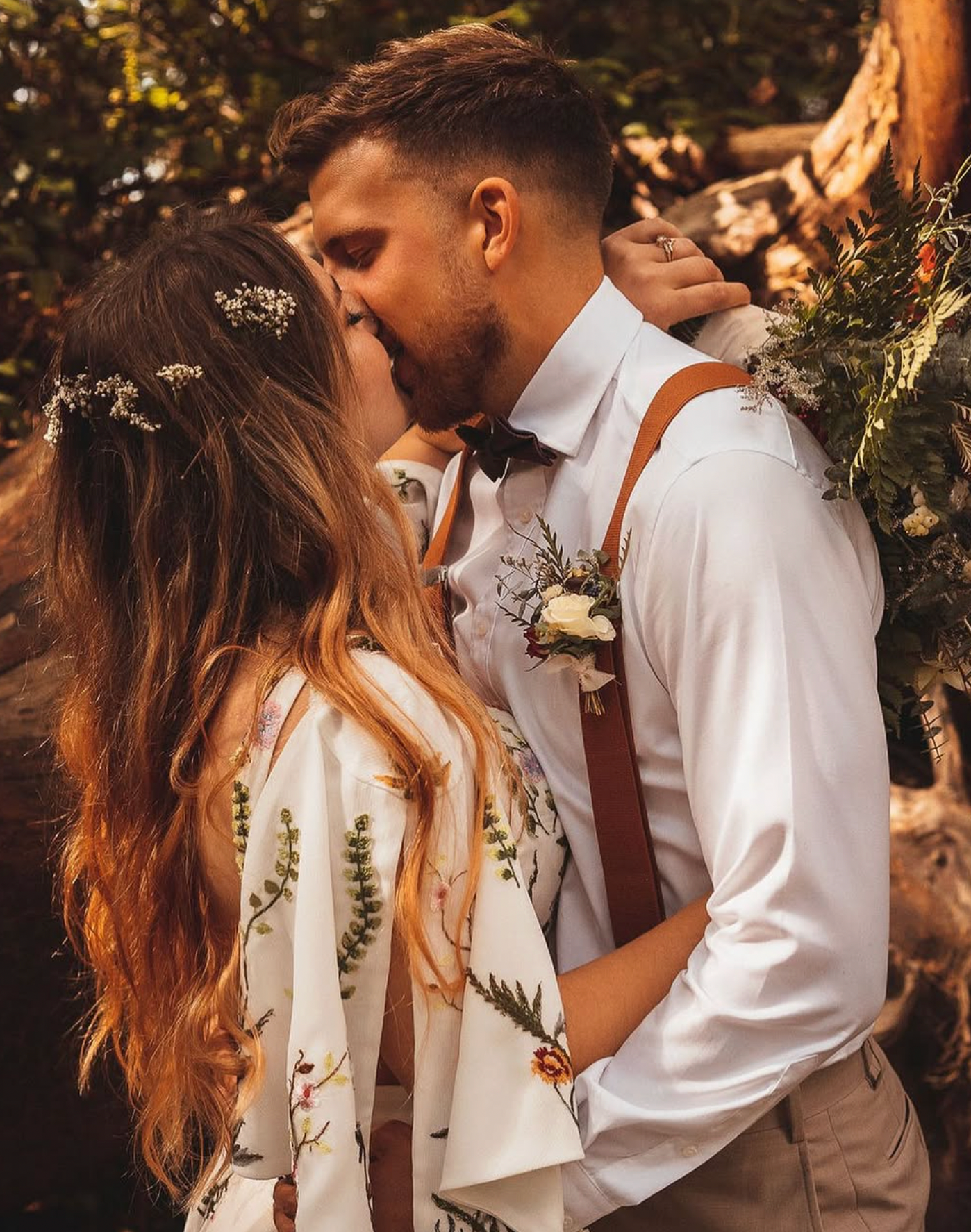 Bride and groom share a kiss outdoors, bride wearing floral dress with baby breath hair crown.