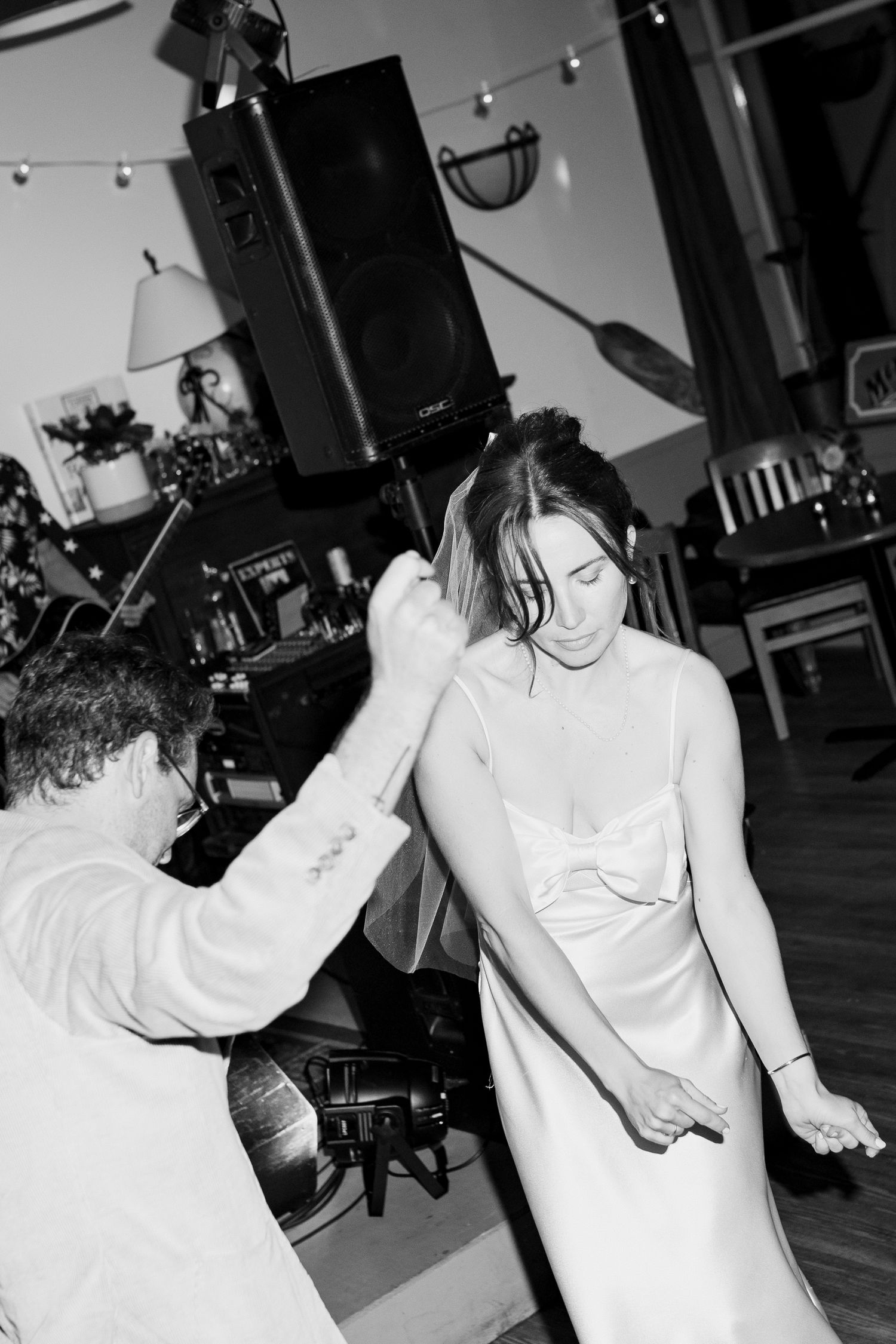 Black and white photo of bride in satin gown being spun by partner on wedding dance floor.