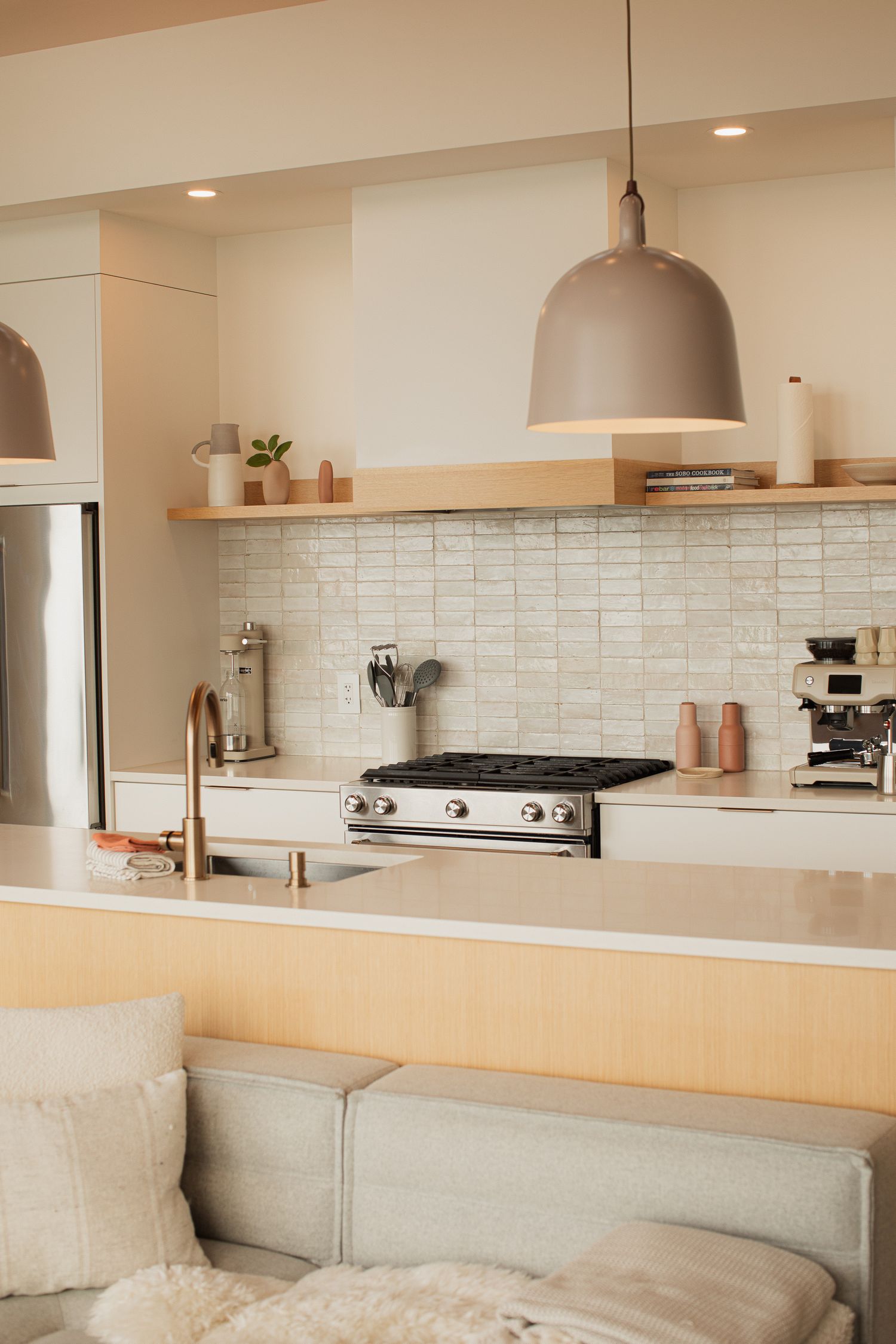Bright modern kitchen with tile backsplash, open shelving, gas range, and large pendant light.