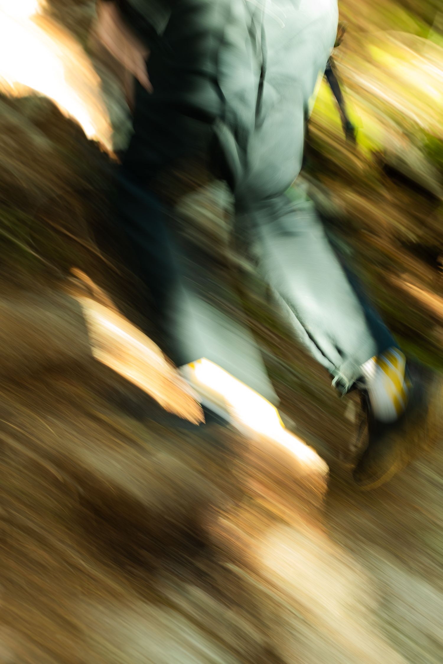 Motion blur photo of hiker walking through autumn forest trail wearing gray jacket and yellow-accented boots.