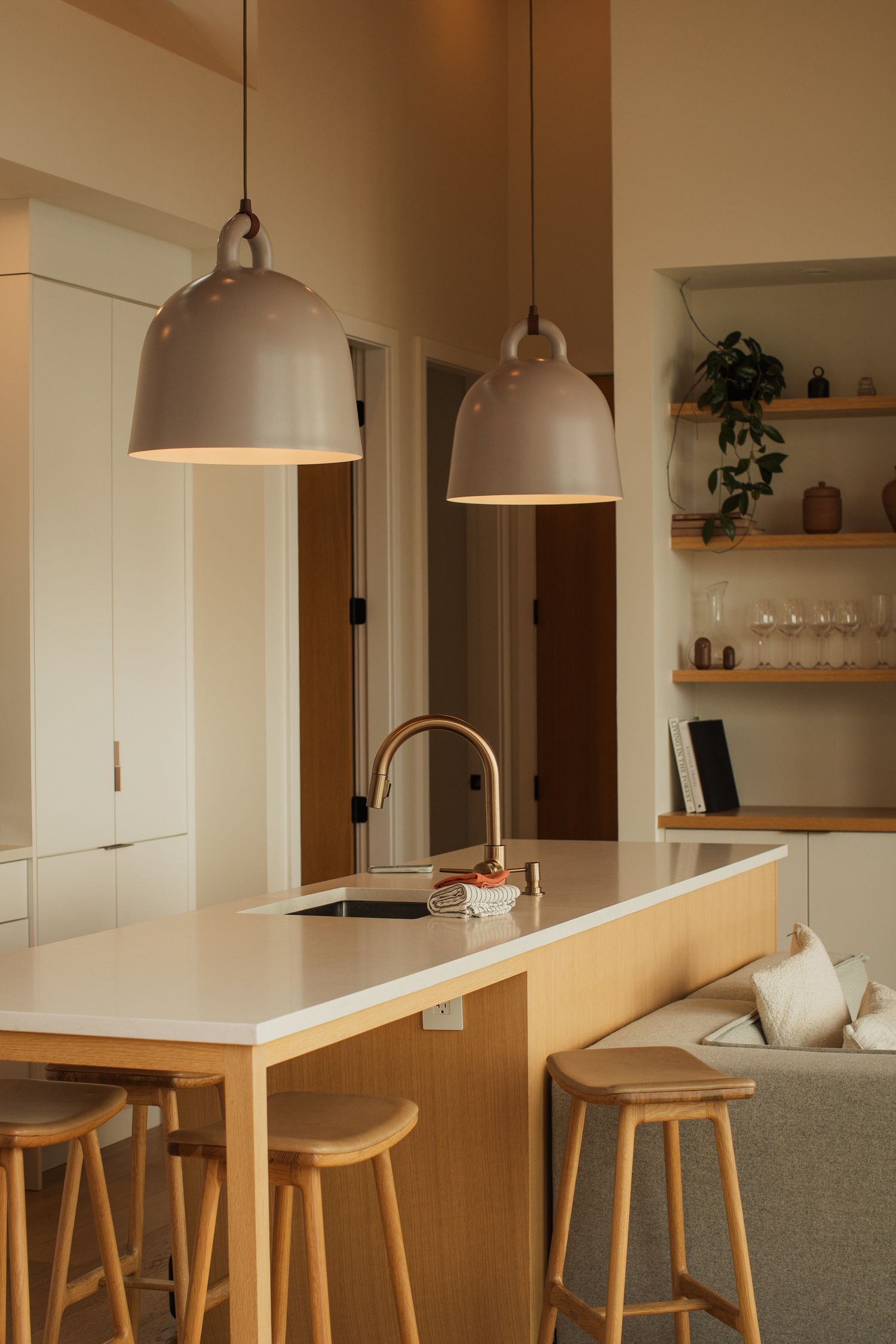 Modern Scandinavian kitchen island with white countertop, wood barstools, and large pendant lights.