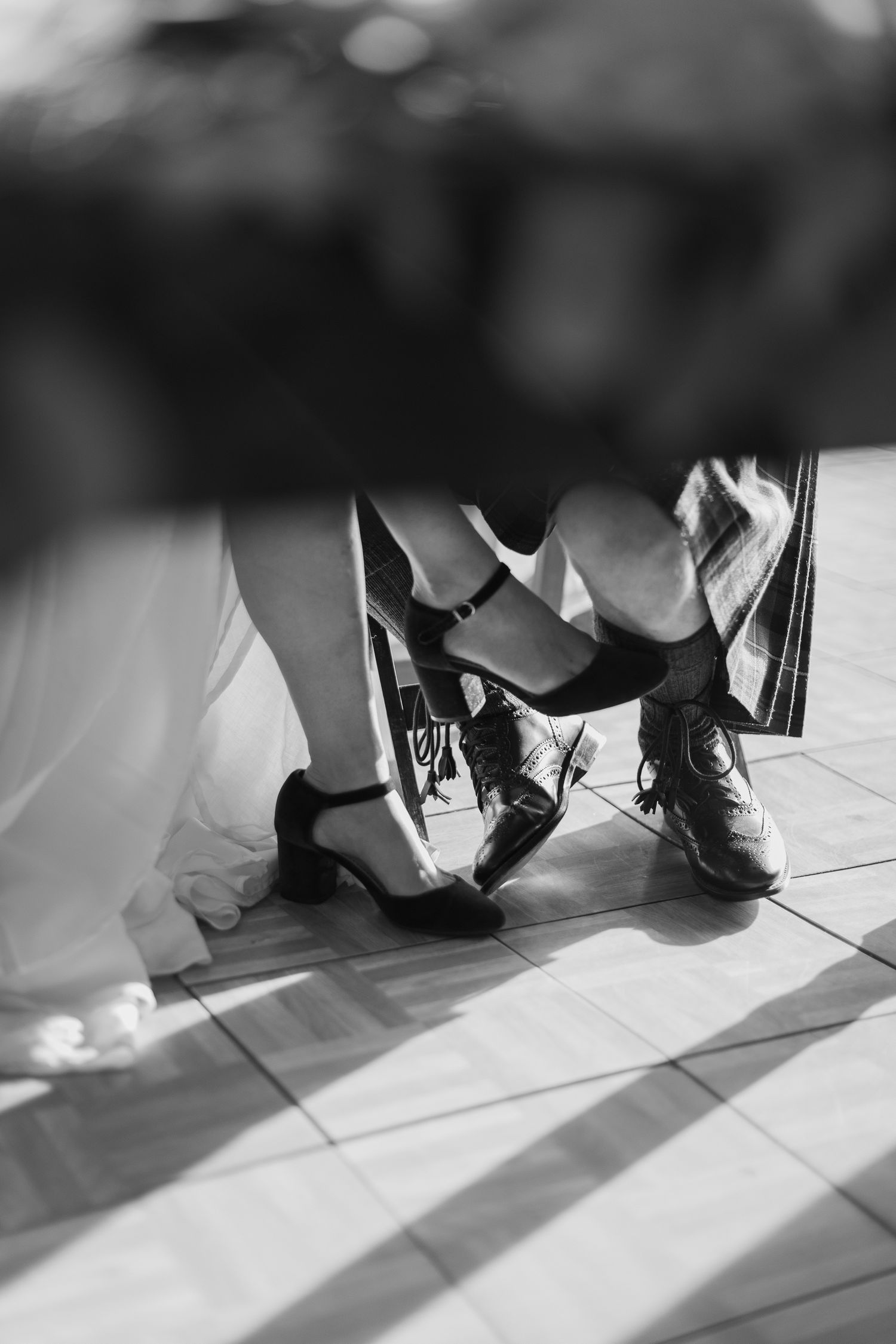 Black and white close-up of bride and groom dancing, showing wedding dress hem and kilted groom's shoes.