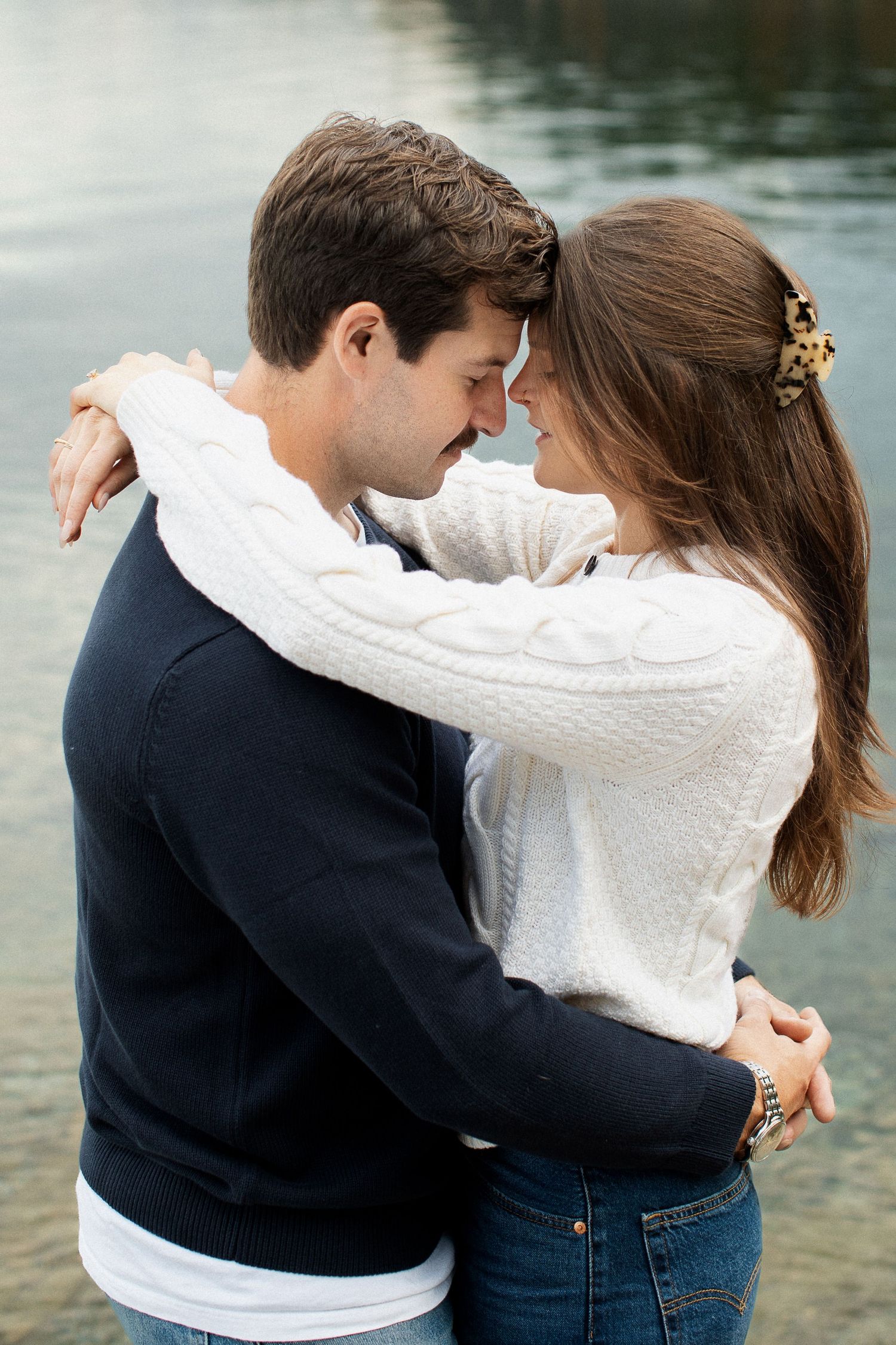 Couple tenderly touching foreheads while embracing near a calm reflective lake.