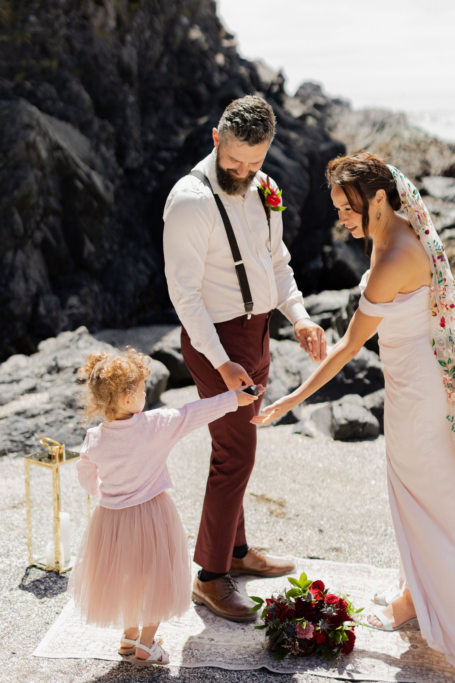 Bride and groom share a tender moment with their young flower girl during a beach wedding ceremony.