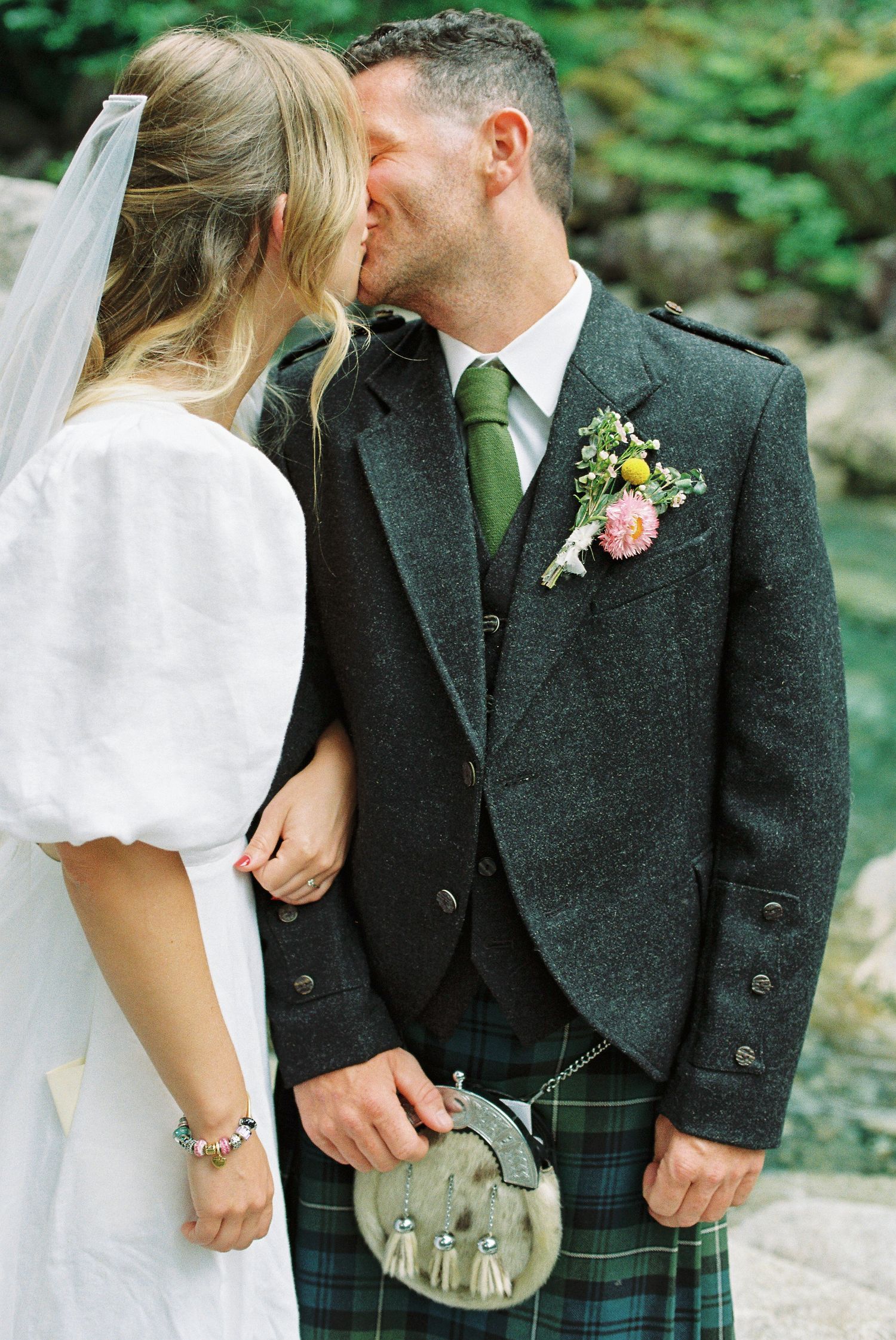 Bride and groom sharing a kiss, groom wearing Scottish tartan kilt with floral boutonniere.