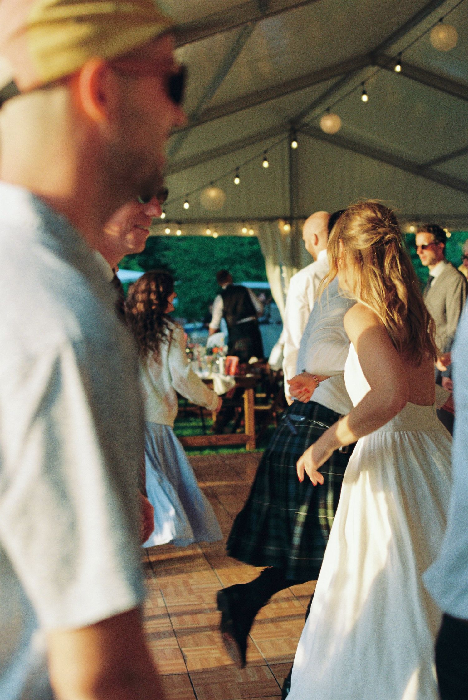 Guests dancing joyfully under a tent at a wedding reception with string lights.