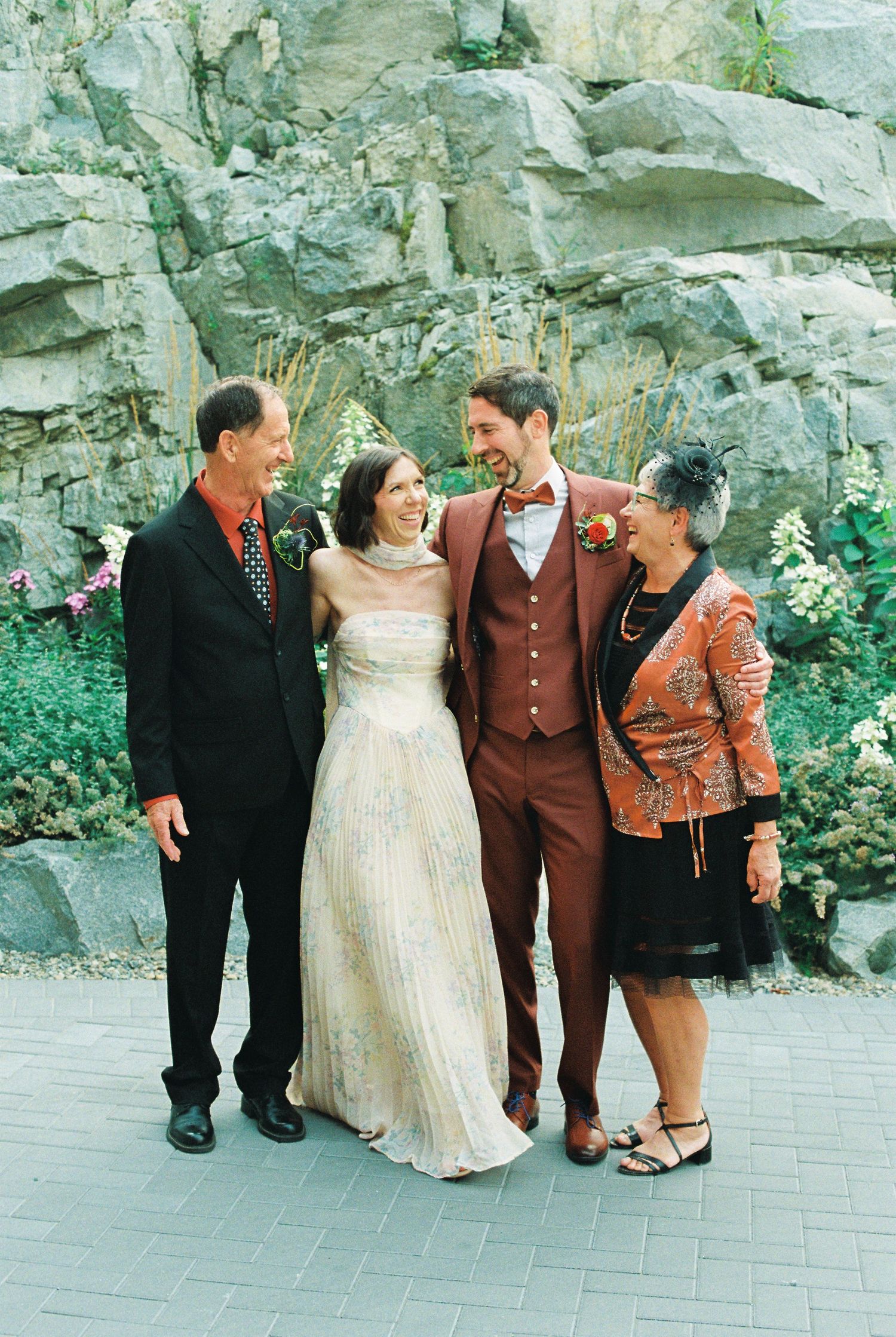 Wedding party of four posing and laughing in front of a rocky backdrop with lush greenery.