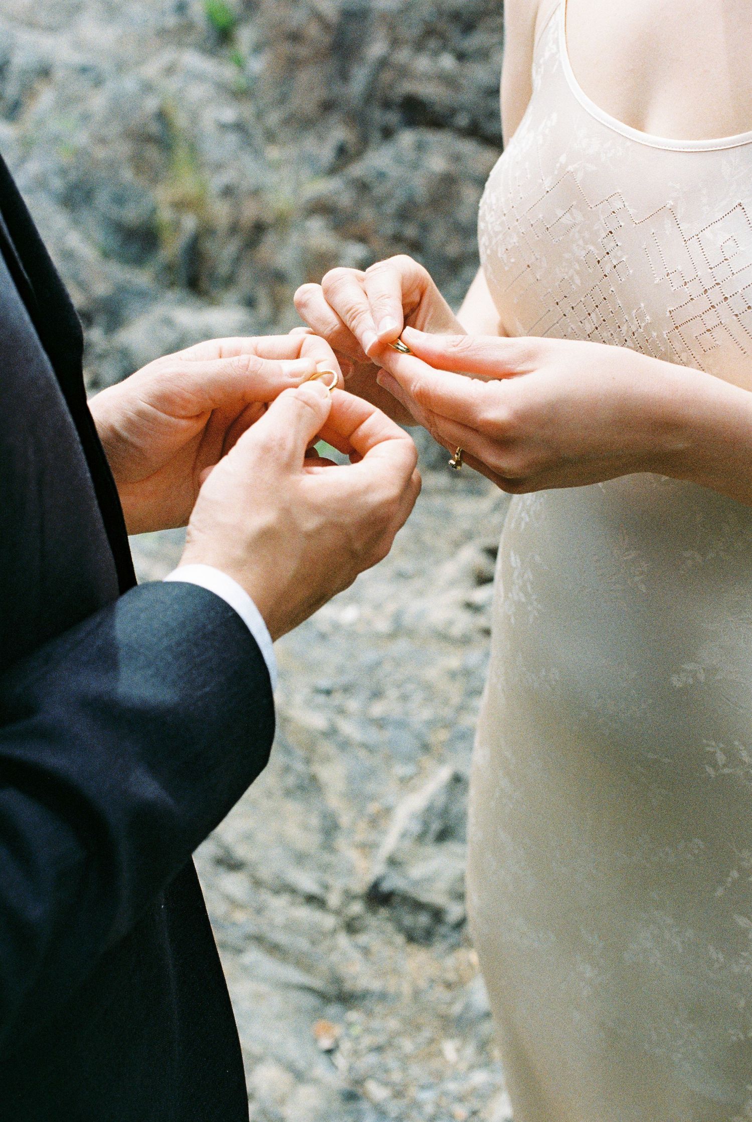 Close-up of bride and groom exchanging wedding rings during outdoor ceremony.