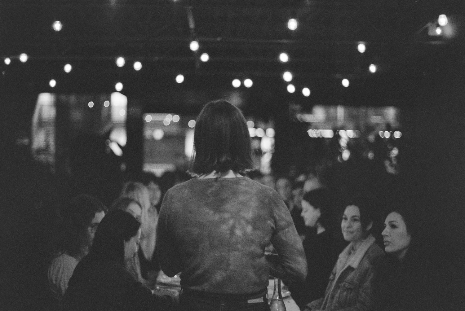 Black and white photo of guests mingling under string lights at an evening party.