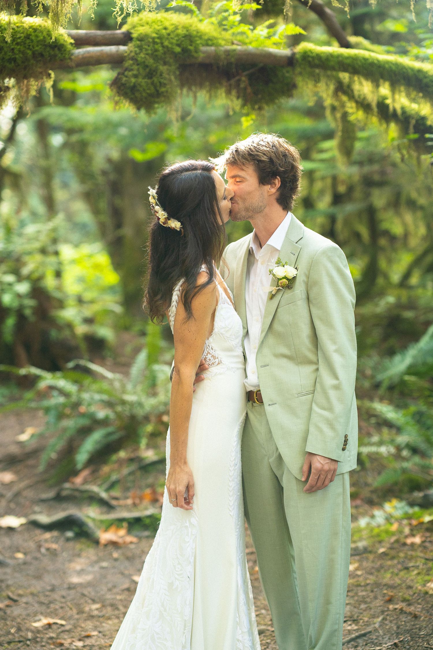 Bride and groom share a kiss in a lush green forest wedding setting.