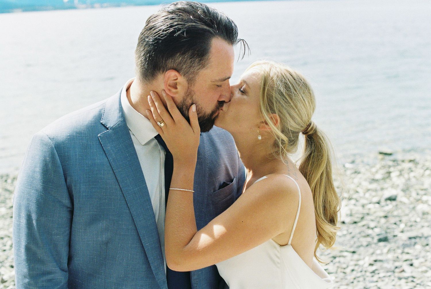 Newlywed couple sharing a romantic kiss on a rocky beach on their wedding day.