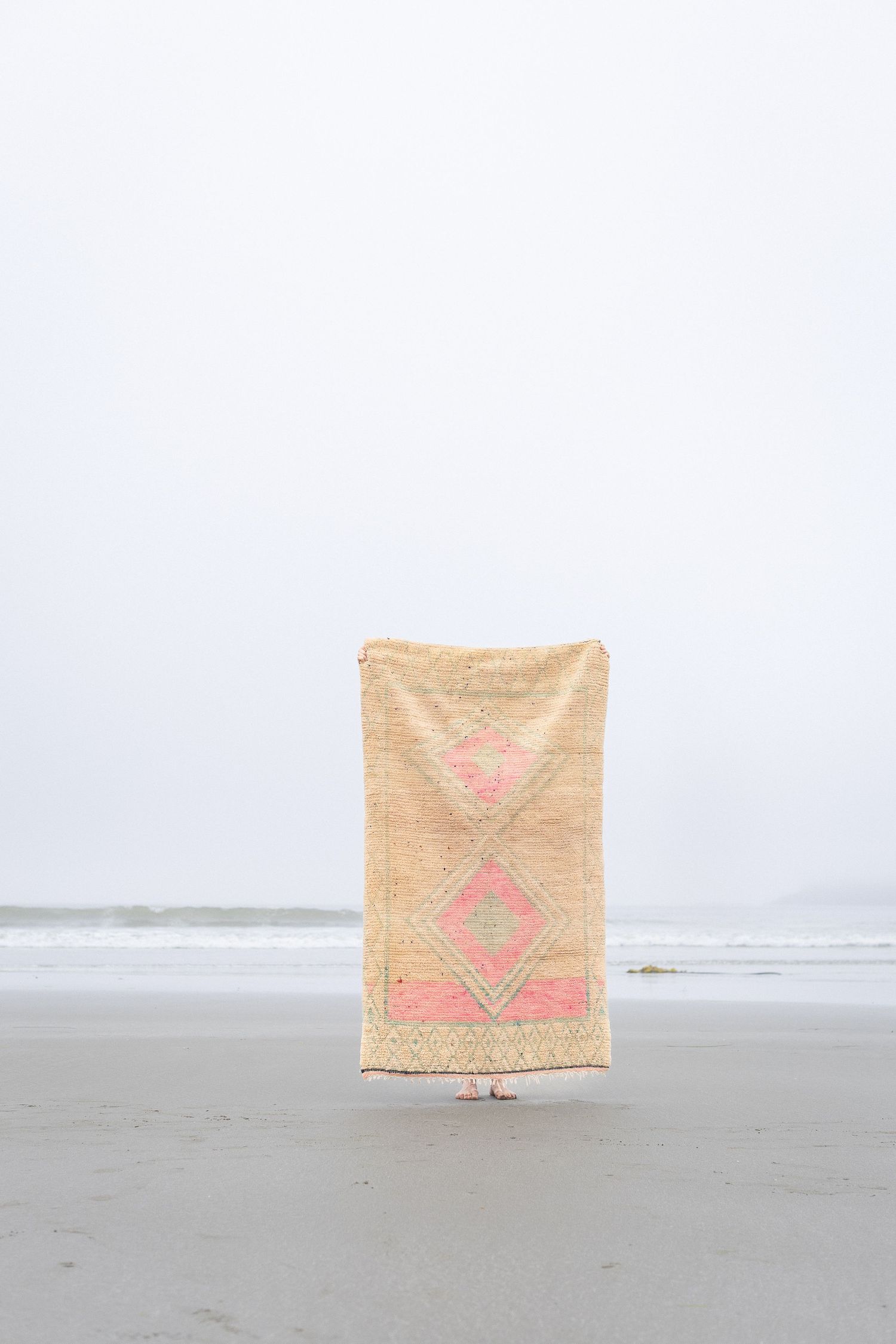 Vintage Moroccan rug with pink geometric pattern displayed on a misty beach.