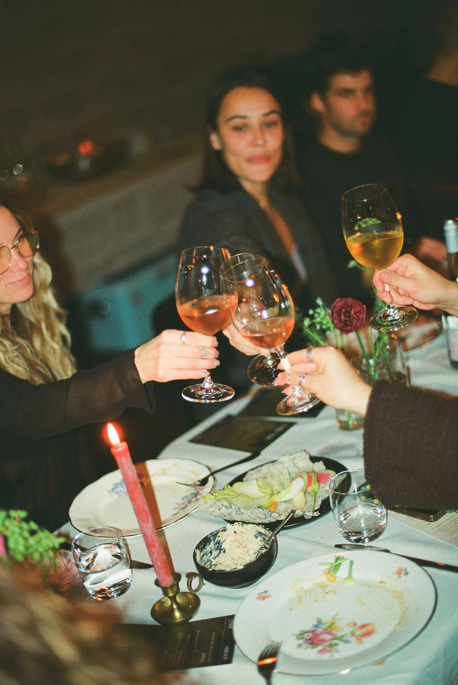 Friends clinking wine glasses in a toast at a candlelit dinner party table.