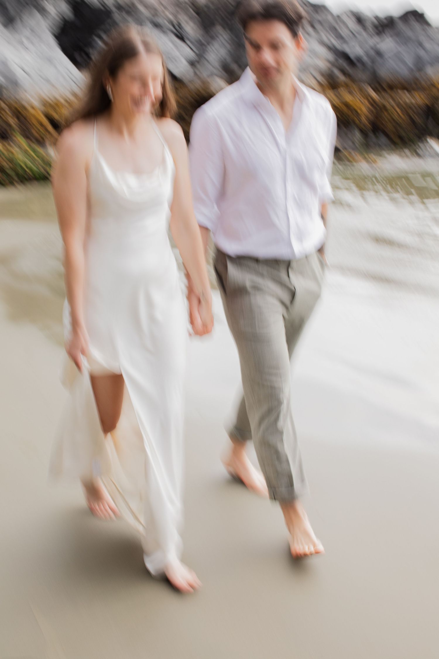 Bride and groom walk barefoot on beach in a romantic motion-blur artistic wedding photo.