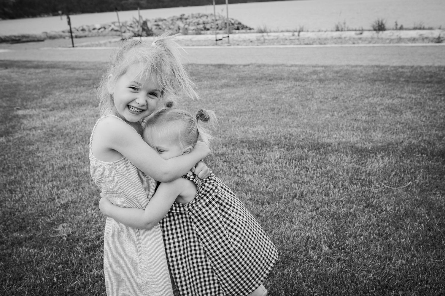 Black and white photo of two young girls hugging and laughing on a grassy lawn.