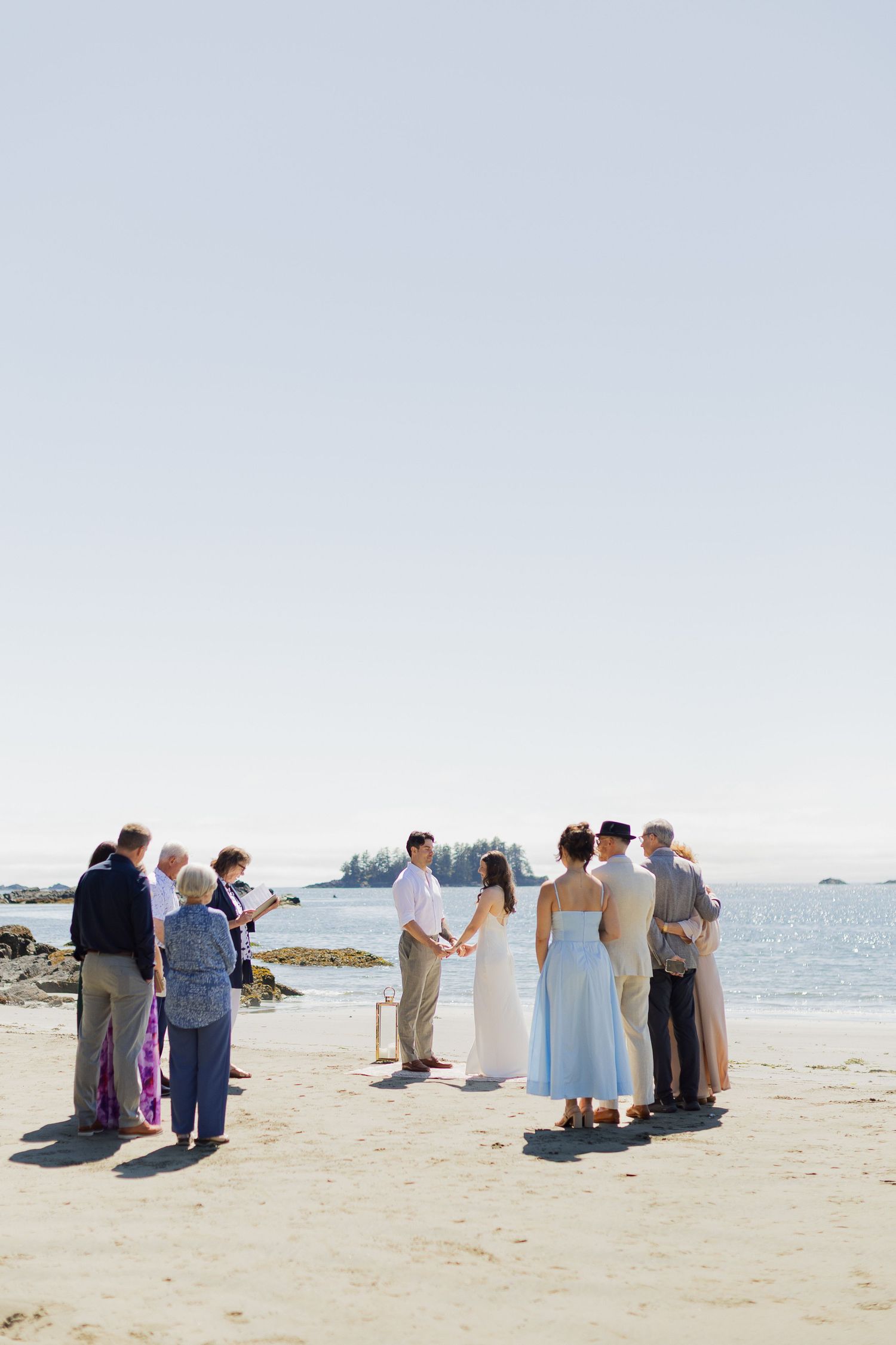 Small intimate beach wedding ceremony with guests gathered by the ocean.