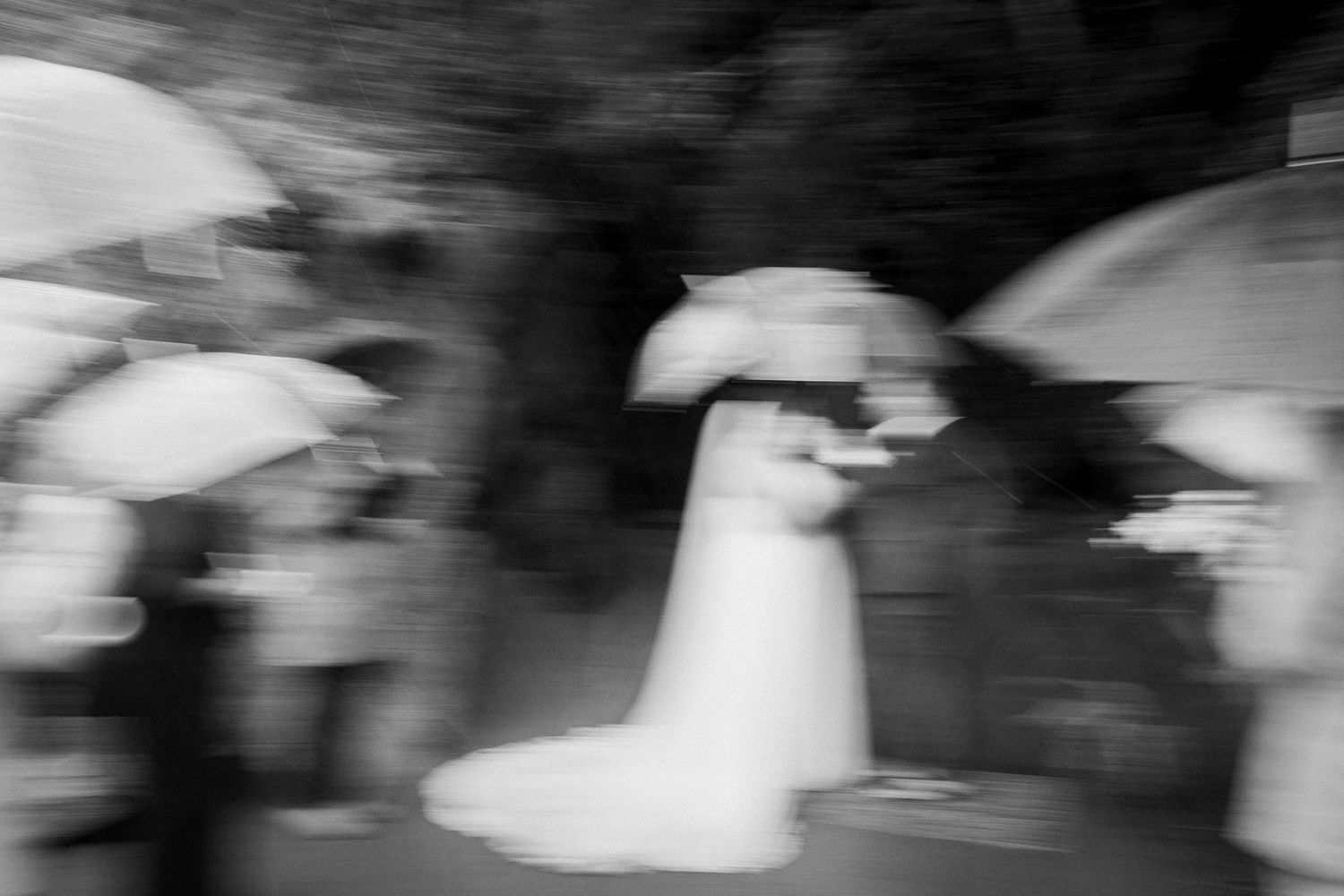 Artistic blurred black and white photo of bride and groom kissing under umbrellas at wedding.