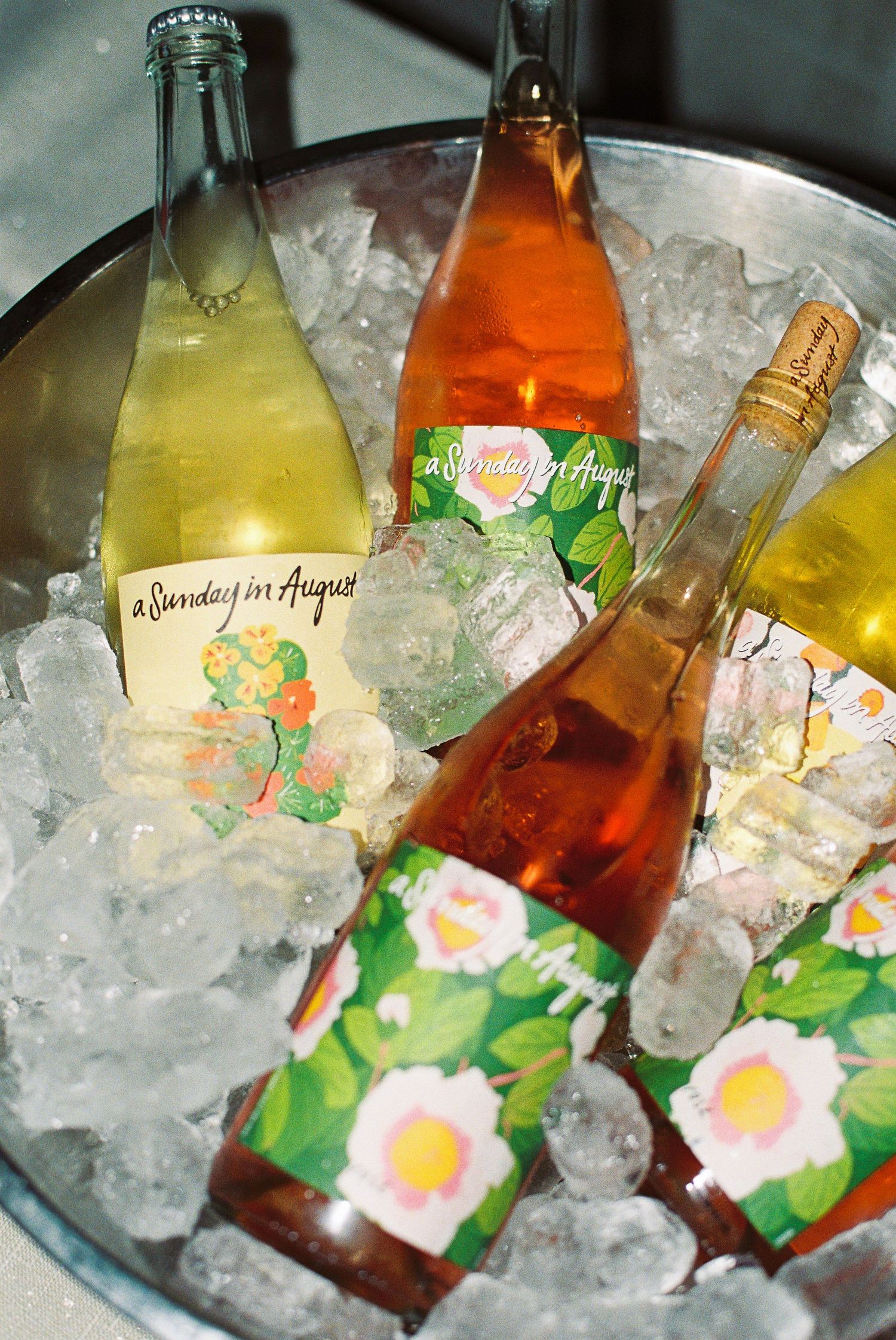 Three bottles of A Sunday in August wine chilling in an ice bucket with floral labels.