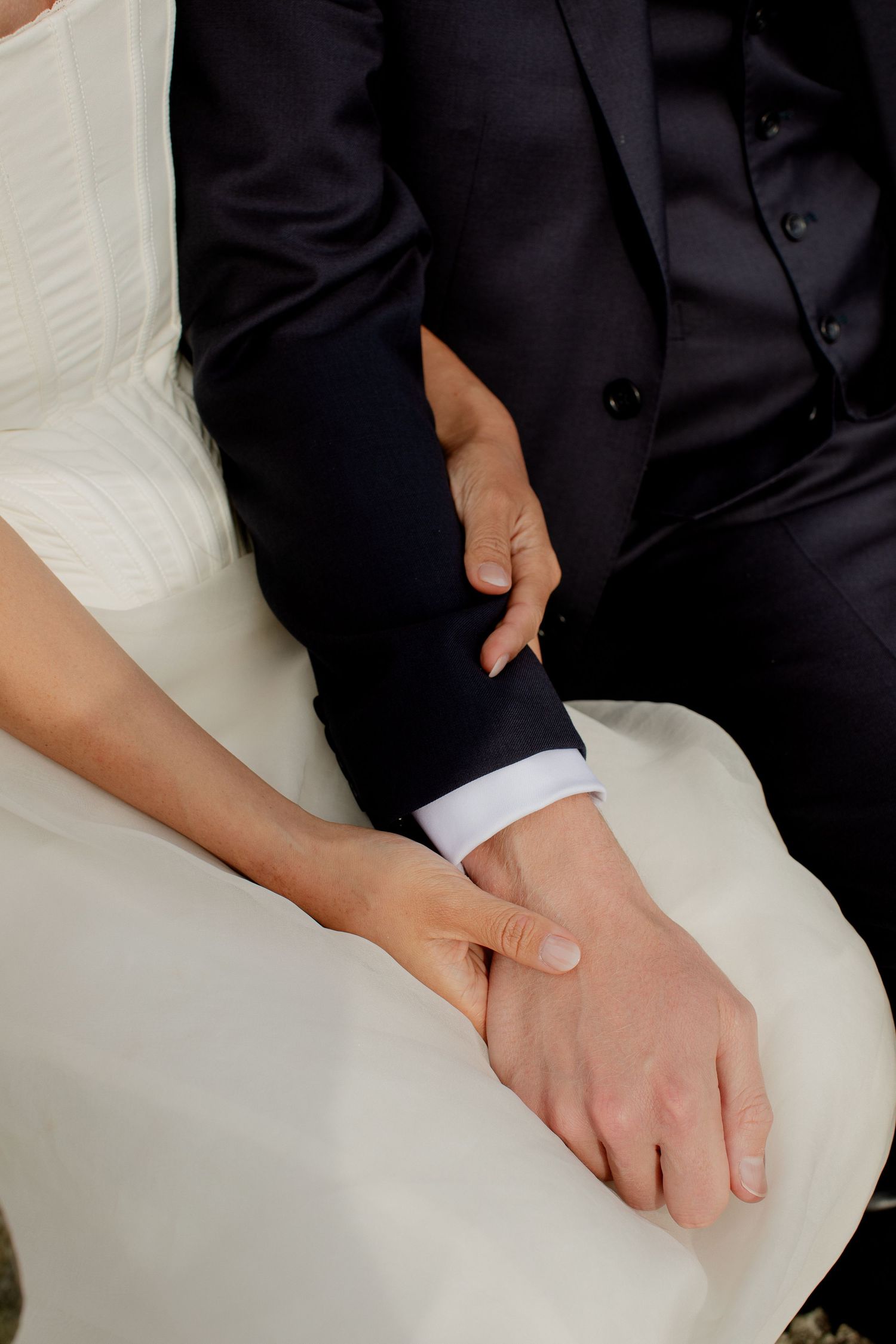 Close-up of bride and groom holding hands, bride in white dress and groom in dark suit.