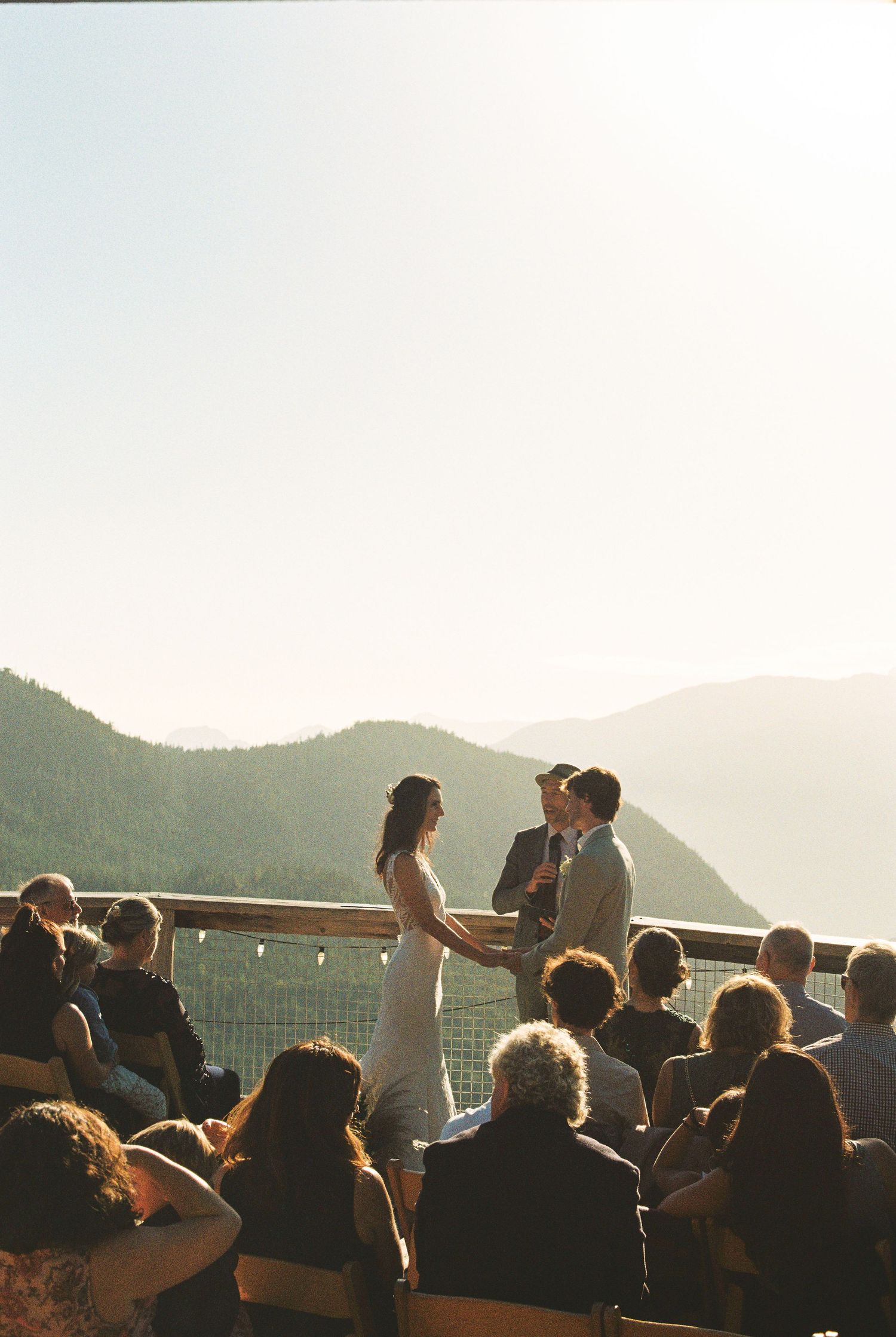 Couple exchanging vows on scenic mountain overlook at golden hour with guests seated below.