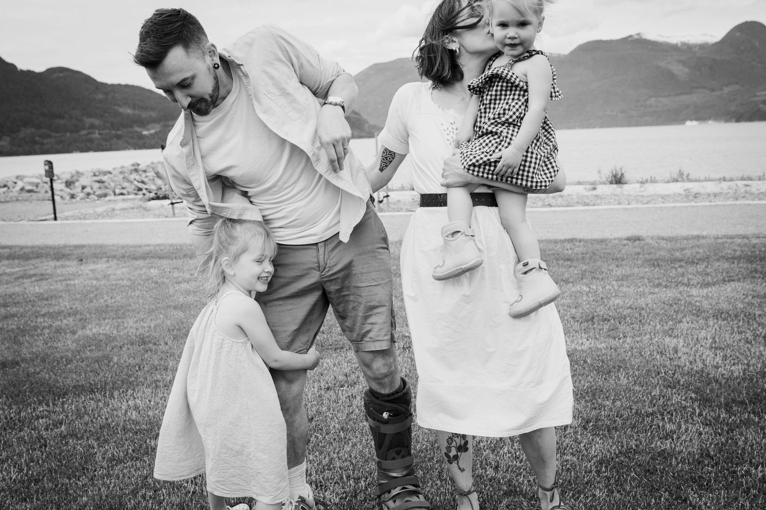 Black and white photo of a family of four playing and laughing together on a lawn.