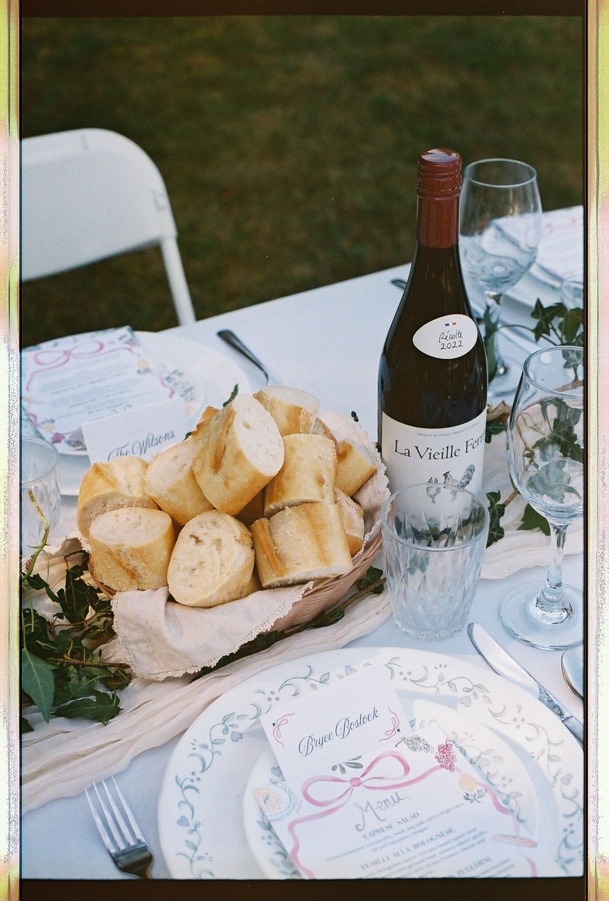 Elegant outdoor wedding table setting with bread basket, wine bottle, and decorative place settings.