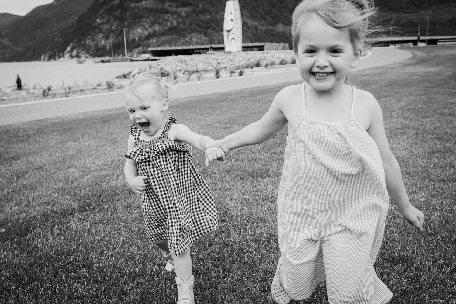 Black and white photo of two little girls holding hands and running joyfully on grass.