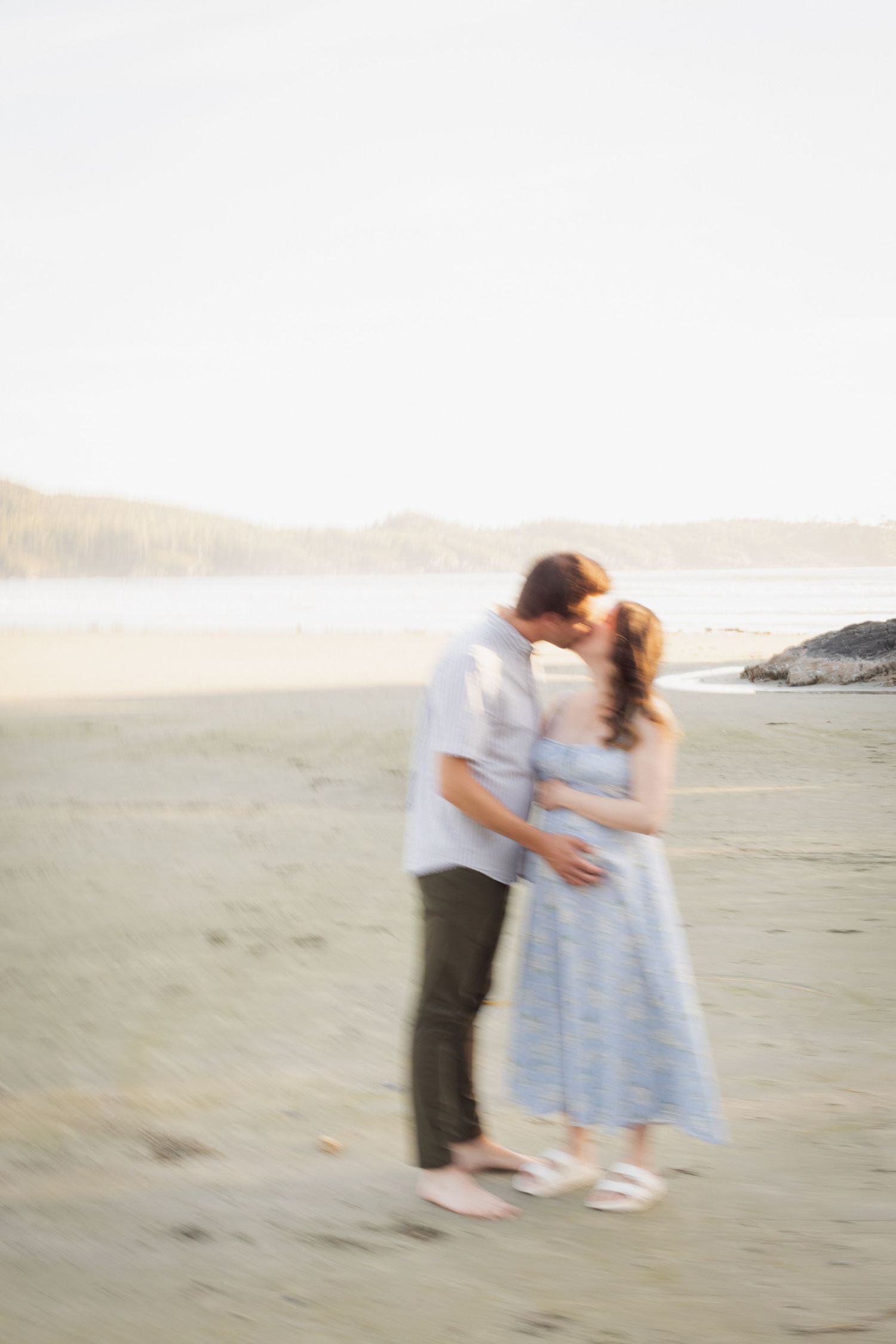 A couple shares a romantic kiss on a sun-drenched beach in a dreamy blurred motion photo.