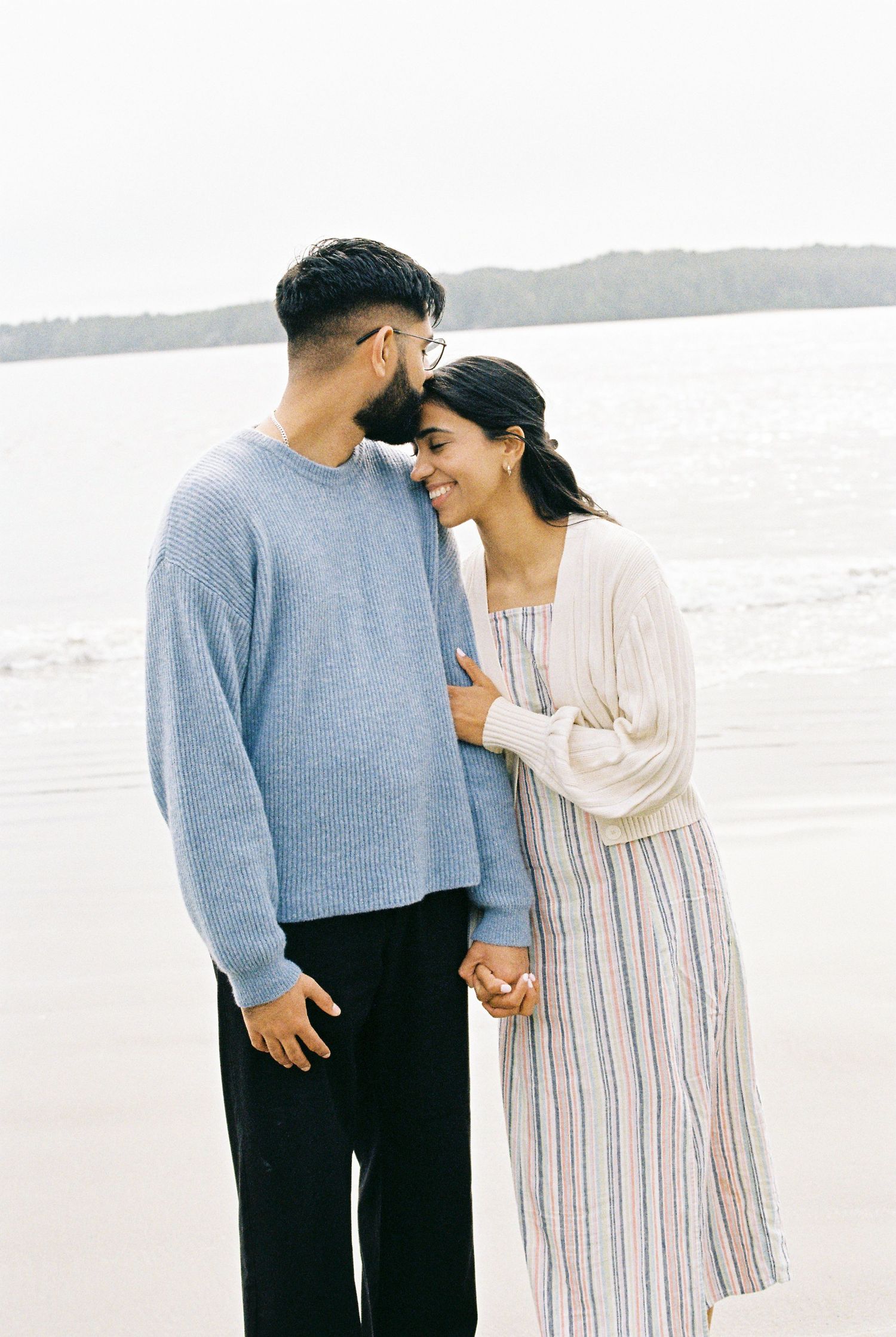 Couple holding hands and sharing a tender moment together on a misty beach.