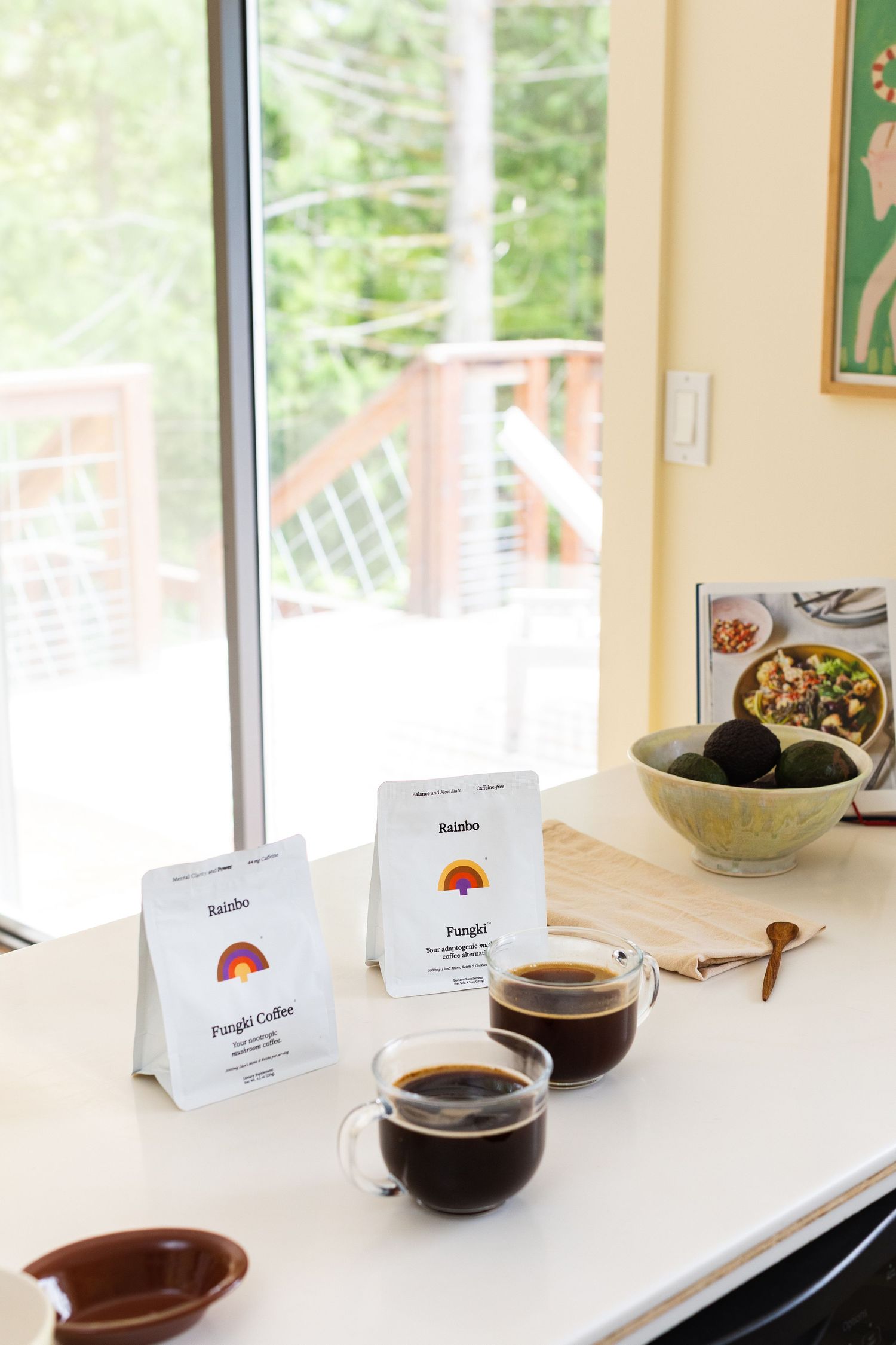 Two glass cups of black coffee with Rainbo Fungi Coffee cards on bright white kitchen counter.
