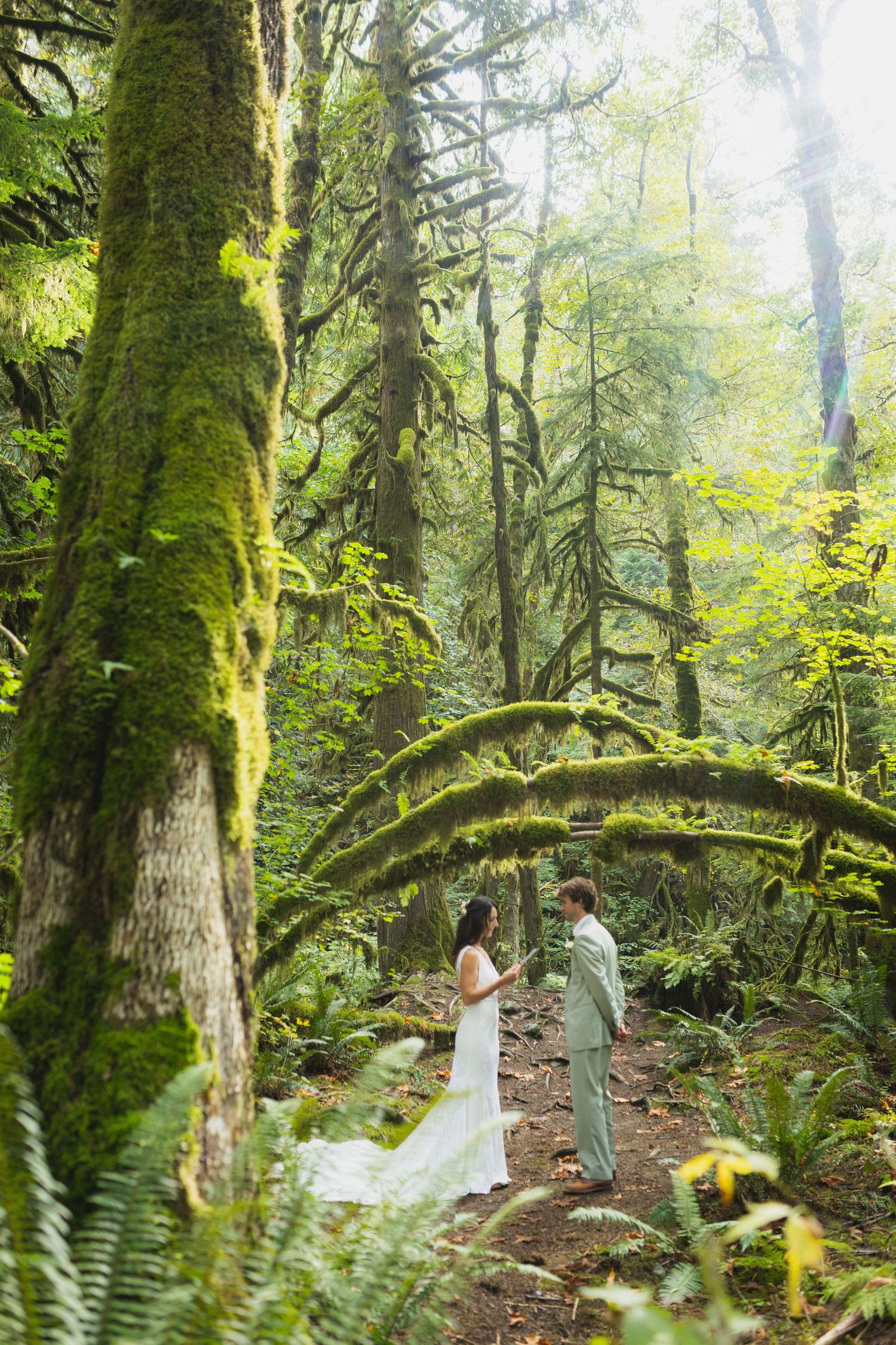 Bride and groom exchange vows in a lush moss-covered Pacific Northwest rainforest setting.