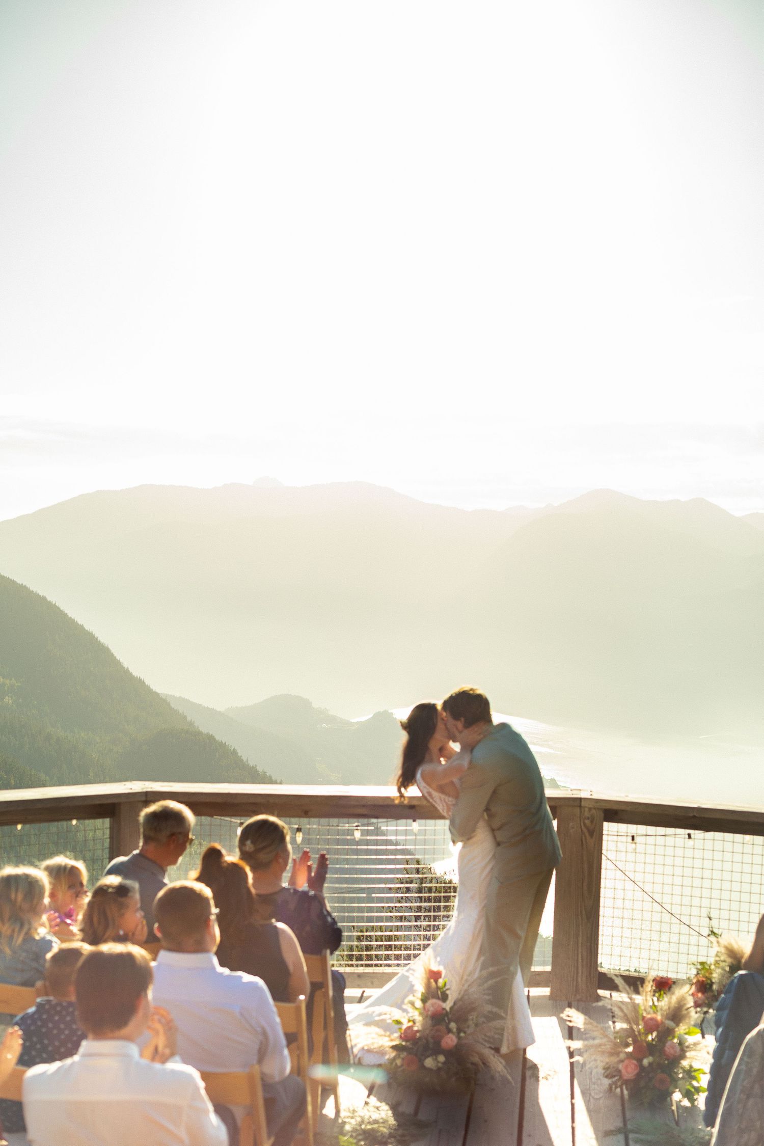 Bride and groom share first kiss on a scenic mountain deck with breathtaking valley views.