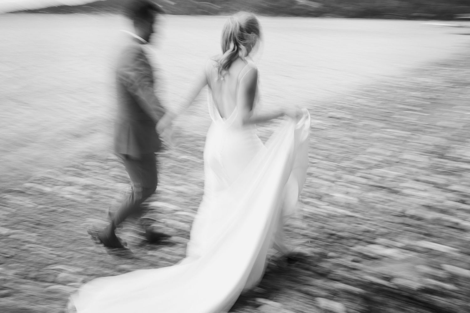 Black and white motion blur photo of bride and groom walking hand in hand on beach.