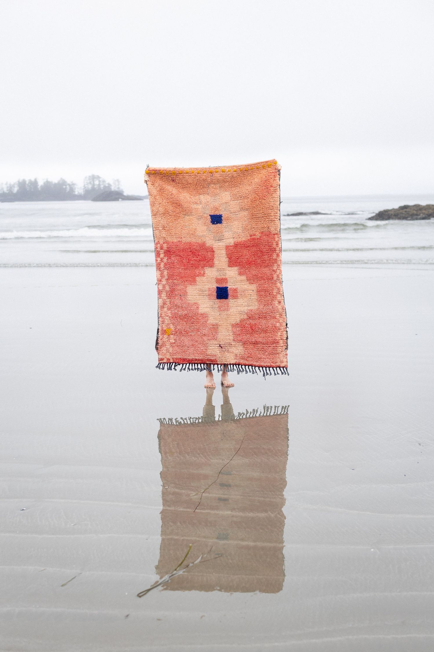 Orange vintage Moroccan rug with blue geometric design reflected on wet beach sand.