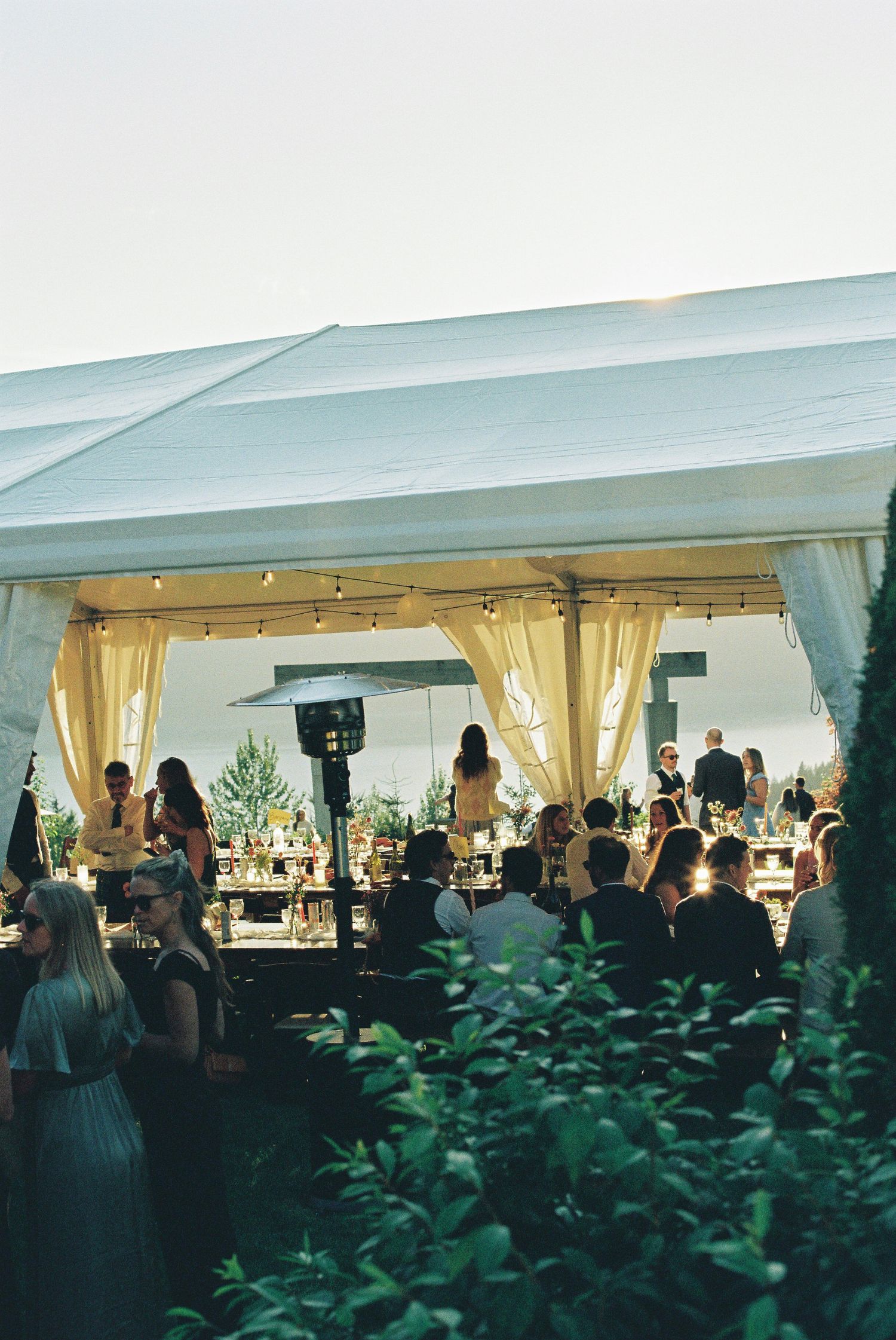 Elegant outdoor wedding reception under a white tent with string lights at dusk.