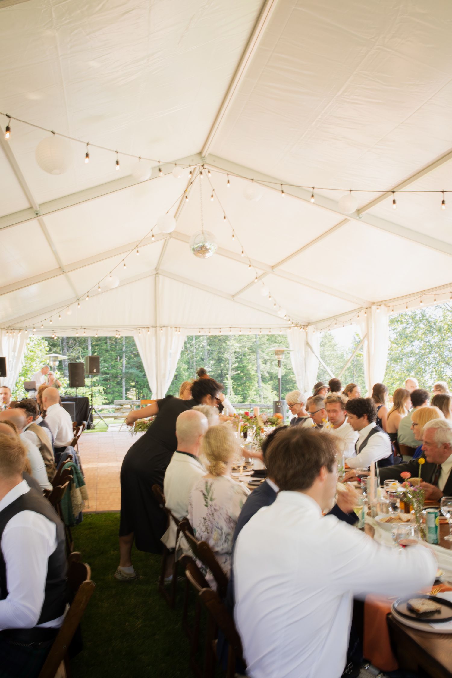 Wedding guests dining under elegant white tent with string lights during indoor reception.