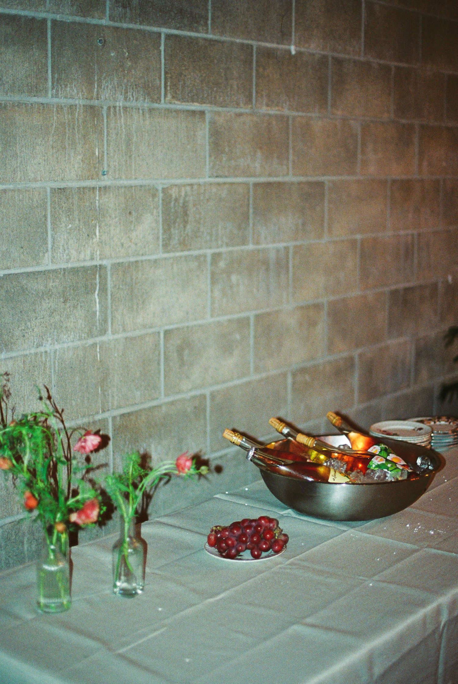 Bottles of wine in a metal ice bucket on a table with flowers against a brick wall.