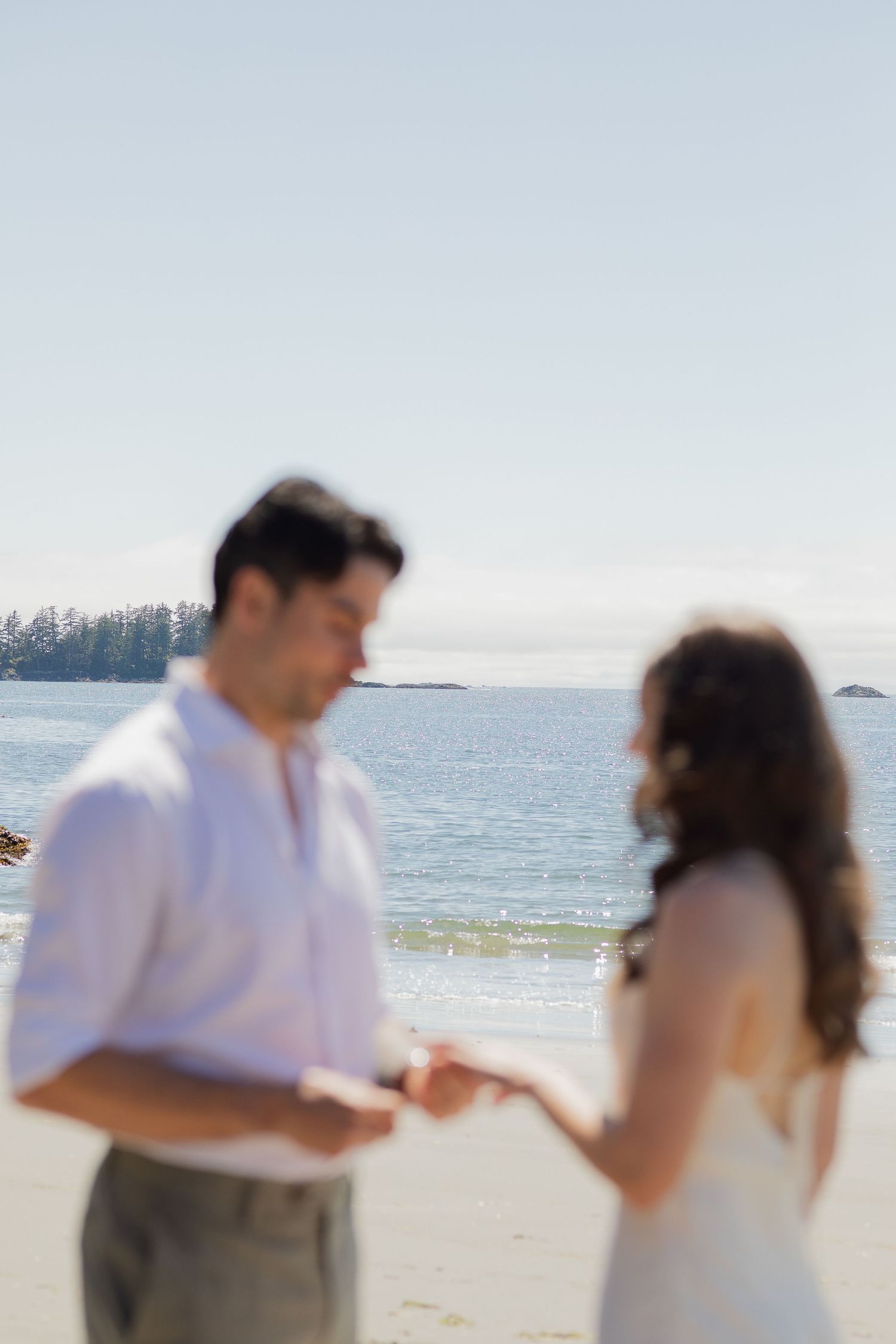 Groom places wedding ring on brides hand during intimate beach ceremony with ocean backdrop.