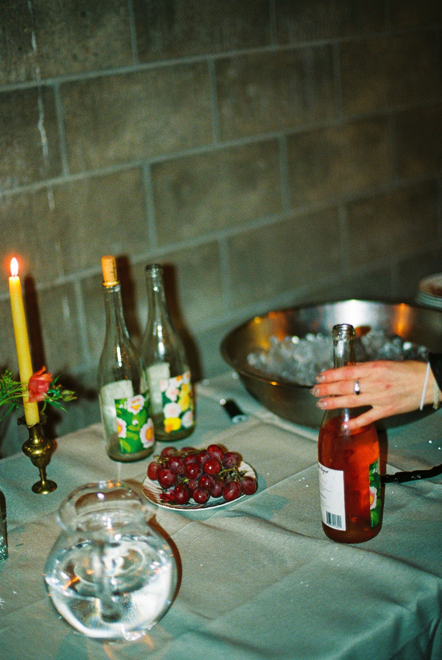 Candles, wine bottles, grapes, and an ice bucket on a table at a dinner party.