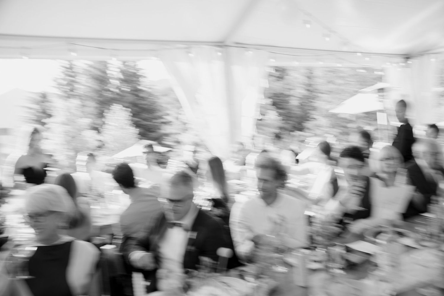 Artistic blurred black and white photo of wedding guests dining and celebrating at a tented reception.