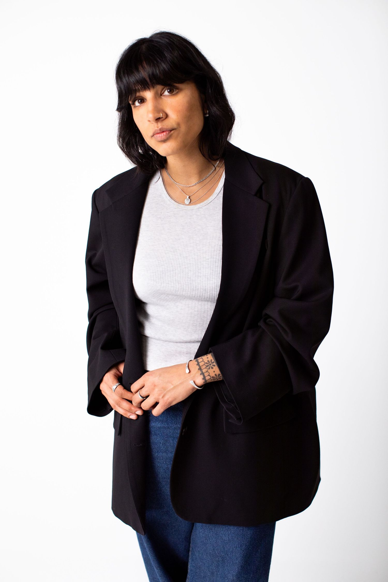 Woman with black bangs wearing oversized black blazer, white top, and jeans on white background.