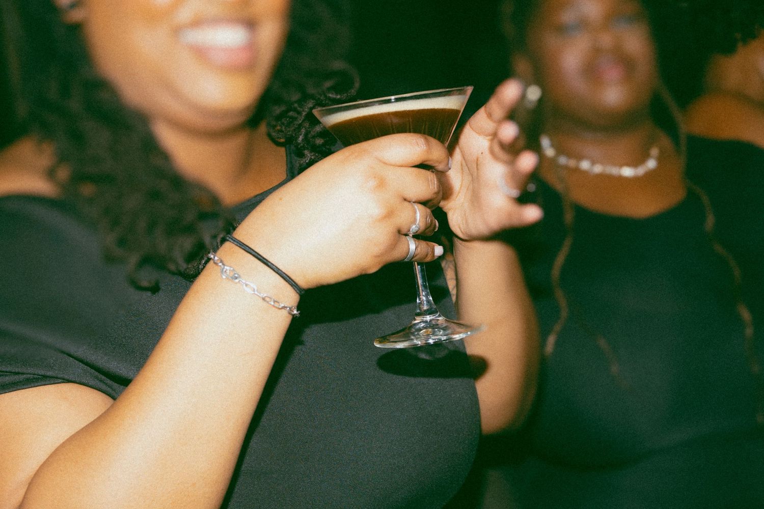 Woman in black dress holding cocktail martini glass at nightclub party event.