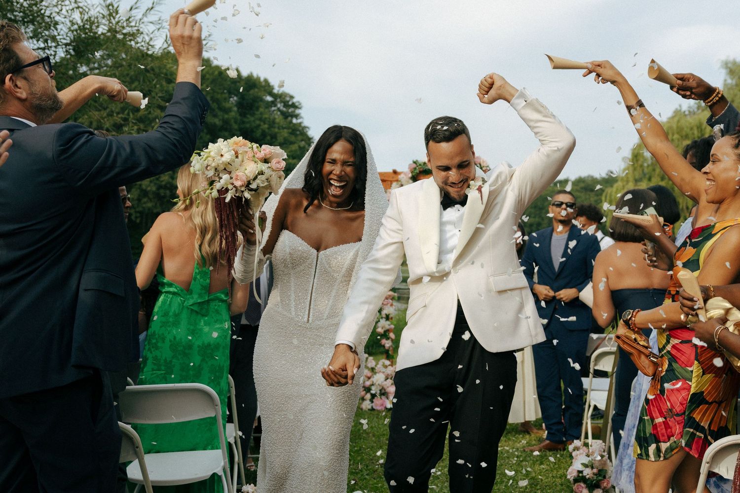 Bride and groom celebrating with confetti during outdoor wedding ceremony recessional.