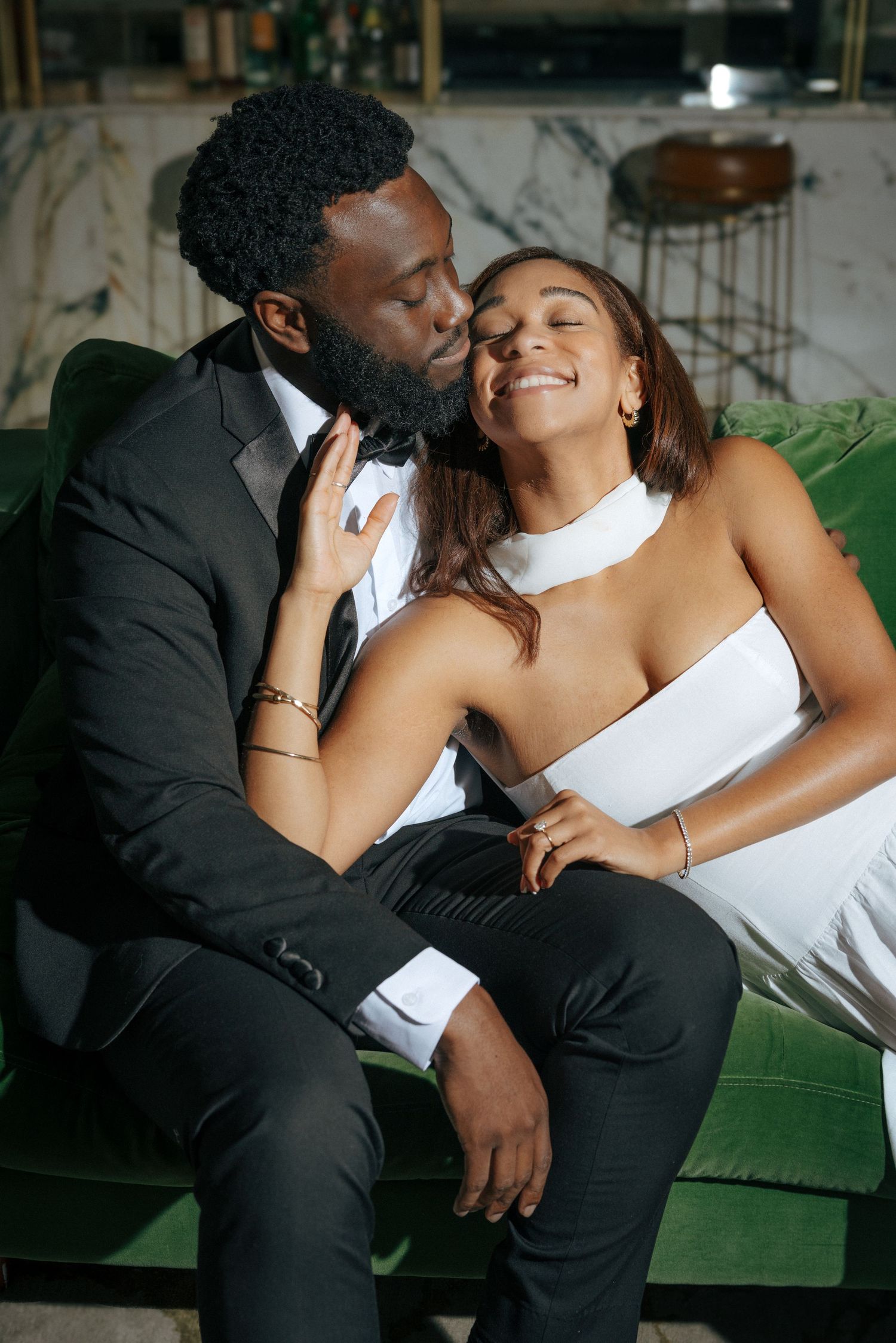 Elegant Black couple in formal wear sharing a romantic moment on a green velvet sofa.