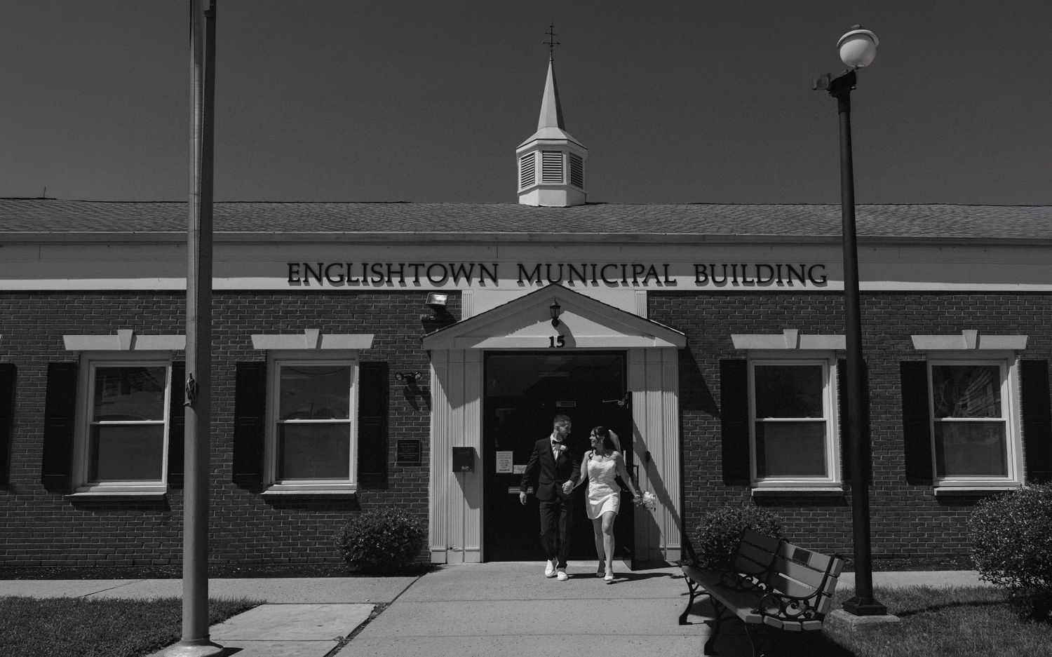 Couple exits Englishtown Municipal Building in black and white wedding photo.