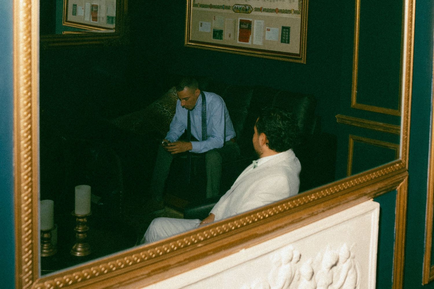 Two people in conversation reflected in a gold-framed mirror, with candles and elegant decor visible.